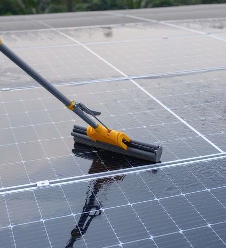 A person is cleaning a solar panel with a broom.