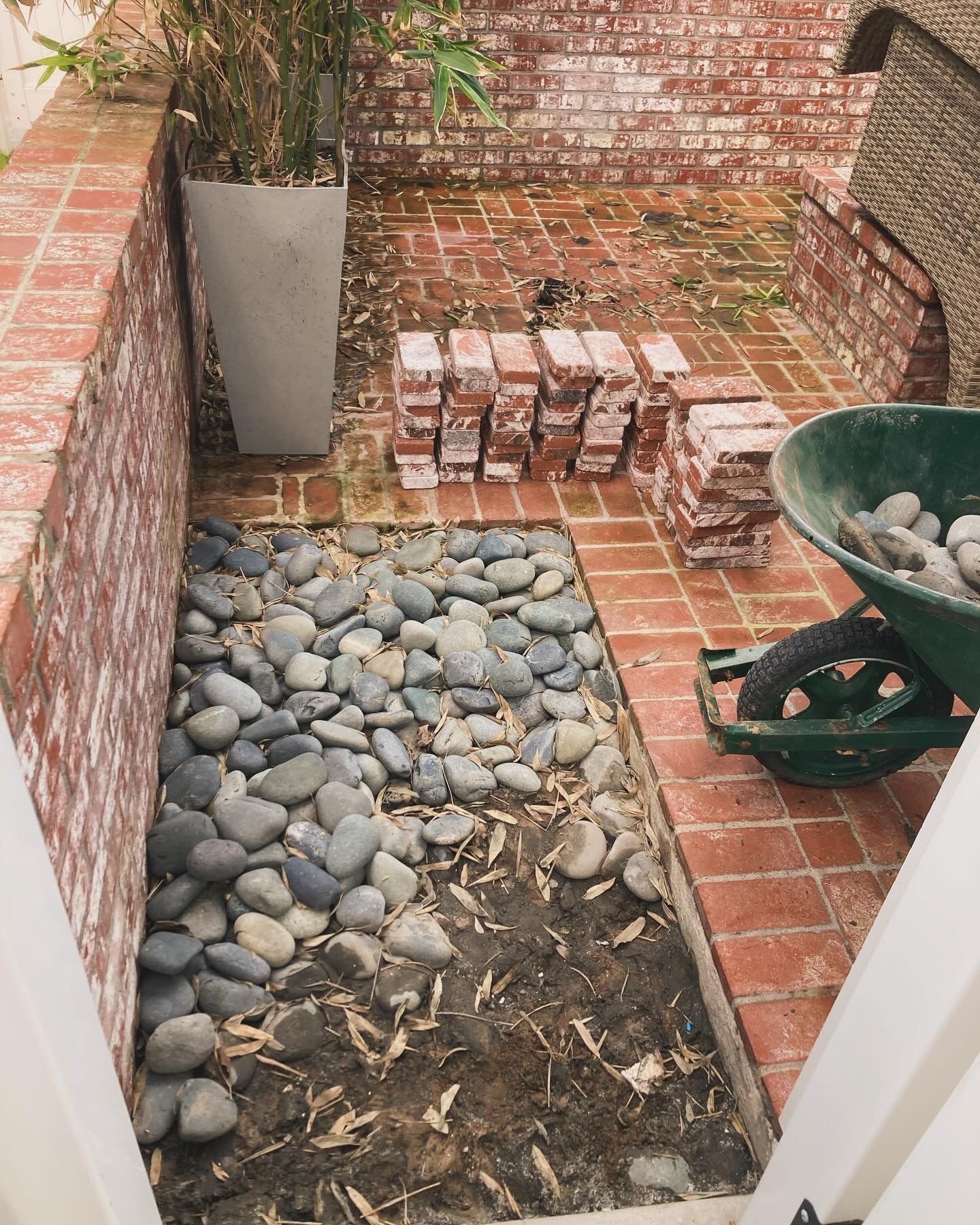 A wheelbarrow filled with rocks is sitting next to a brick wall.