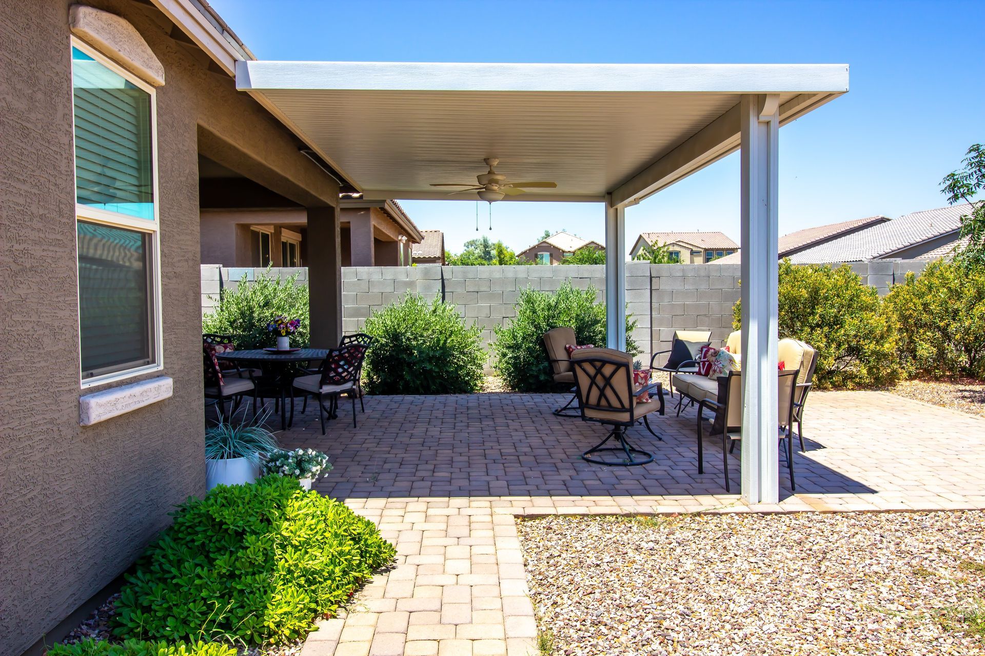 Patio with a white covered structure, outdoor furniture, and brick flooring. Sunny day.