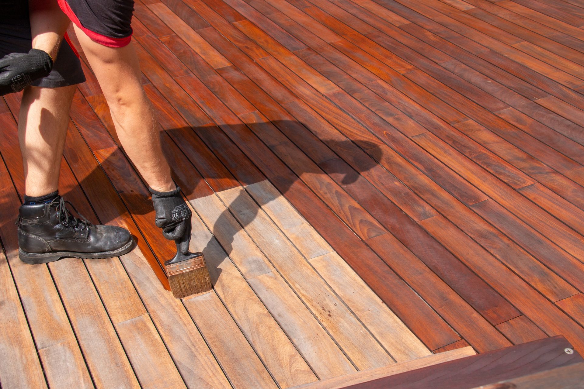 A person is painting a wooden deck with a brush.