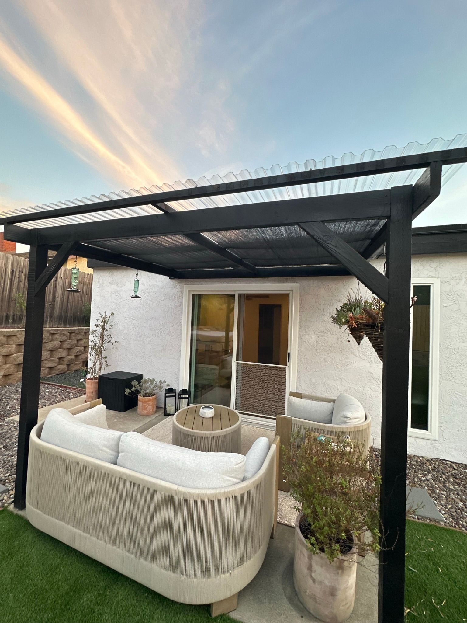 A patio with a couch , chairs , and a fire pit under a pergola.