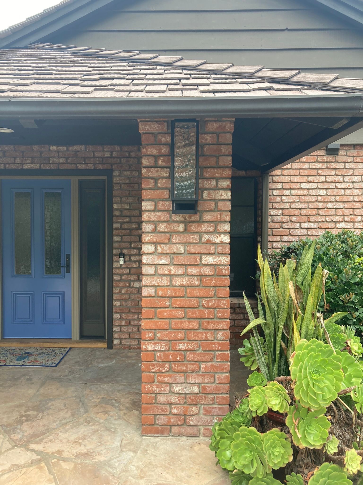 The front of a house with a blue door and a brick pillar