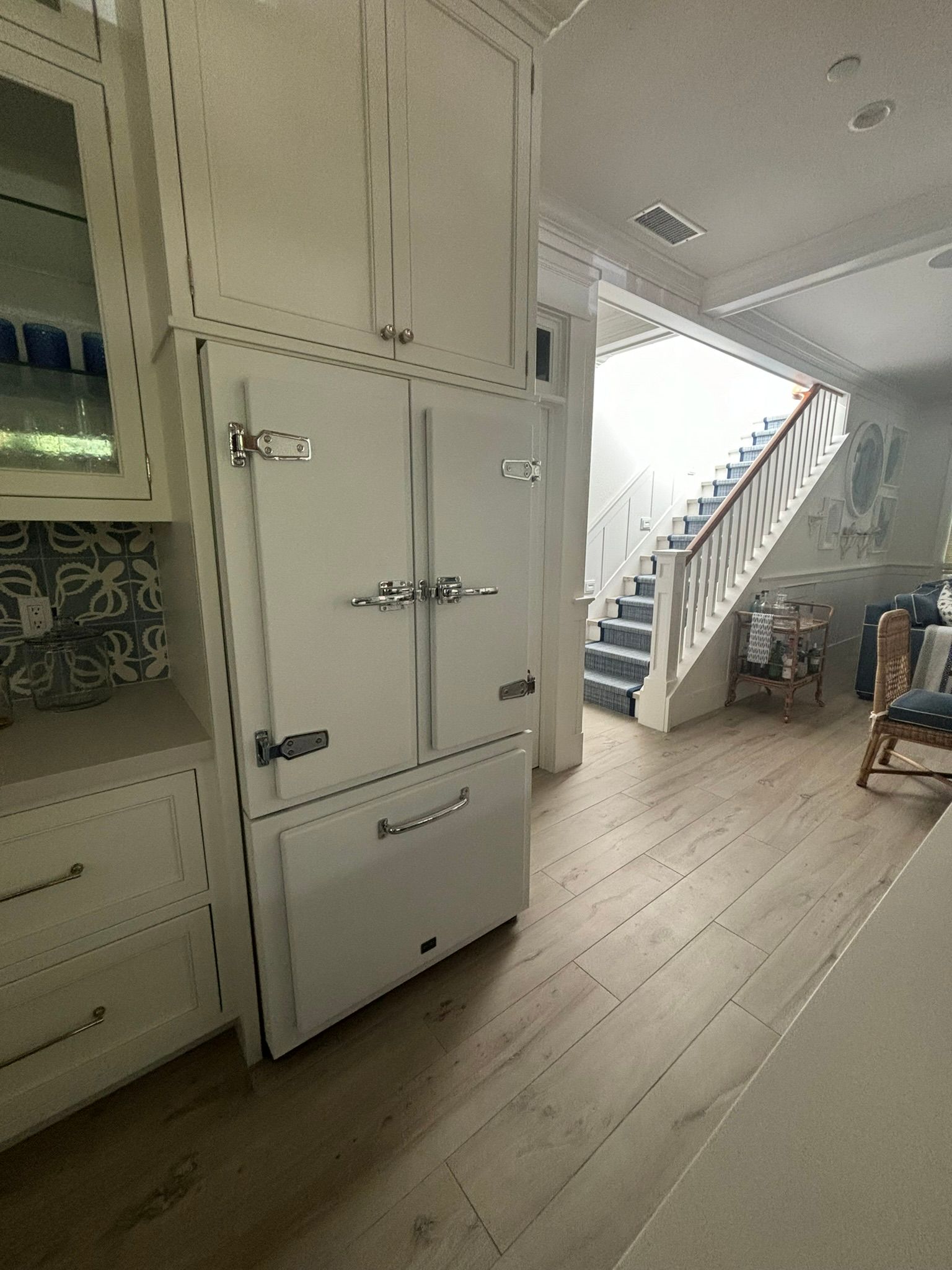 A white refrigerator is sitting in a kitchen next to a staircase.