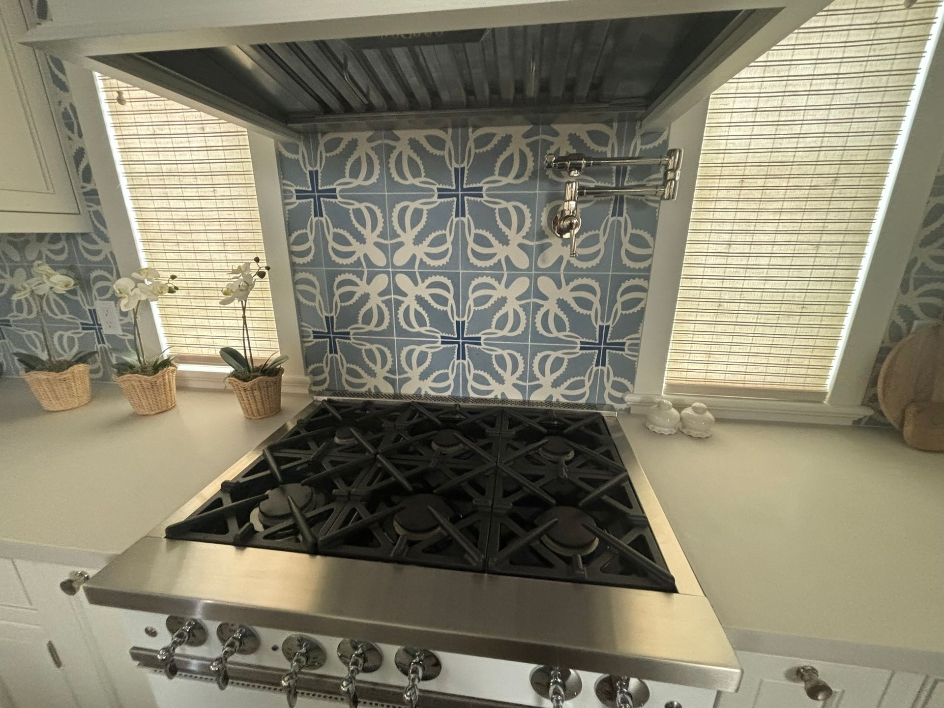 Kitchen stove with blue and white tile backsplash, range hood, and white countertops.