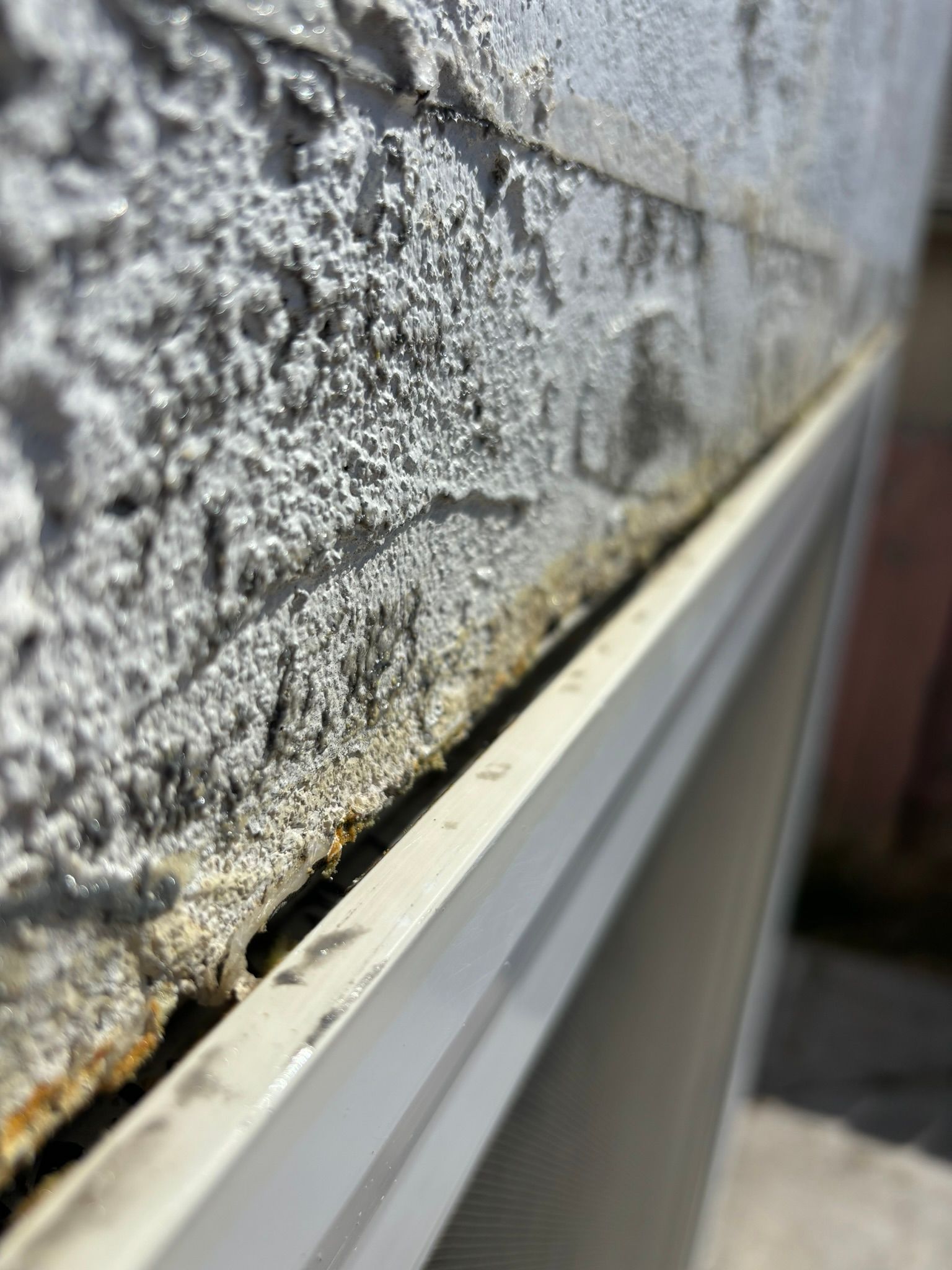 Close-up of a weathered, textured gray wall section with a white frame along the bottom edge, appearing to be an AC unit.