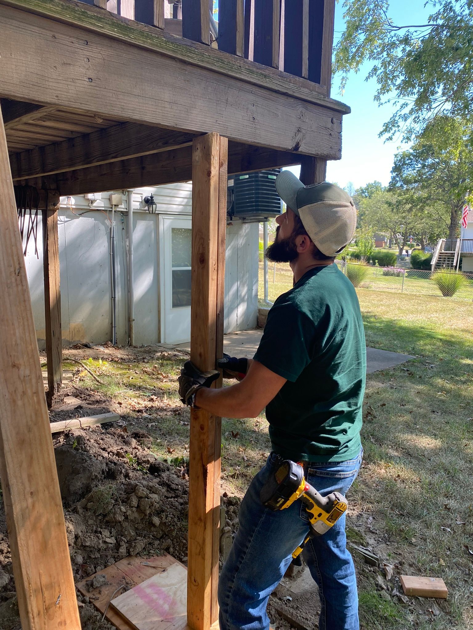 A man is standing next to a wooden post under a deck.