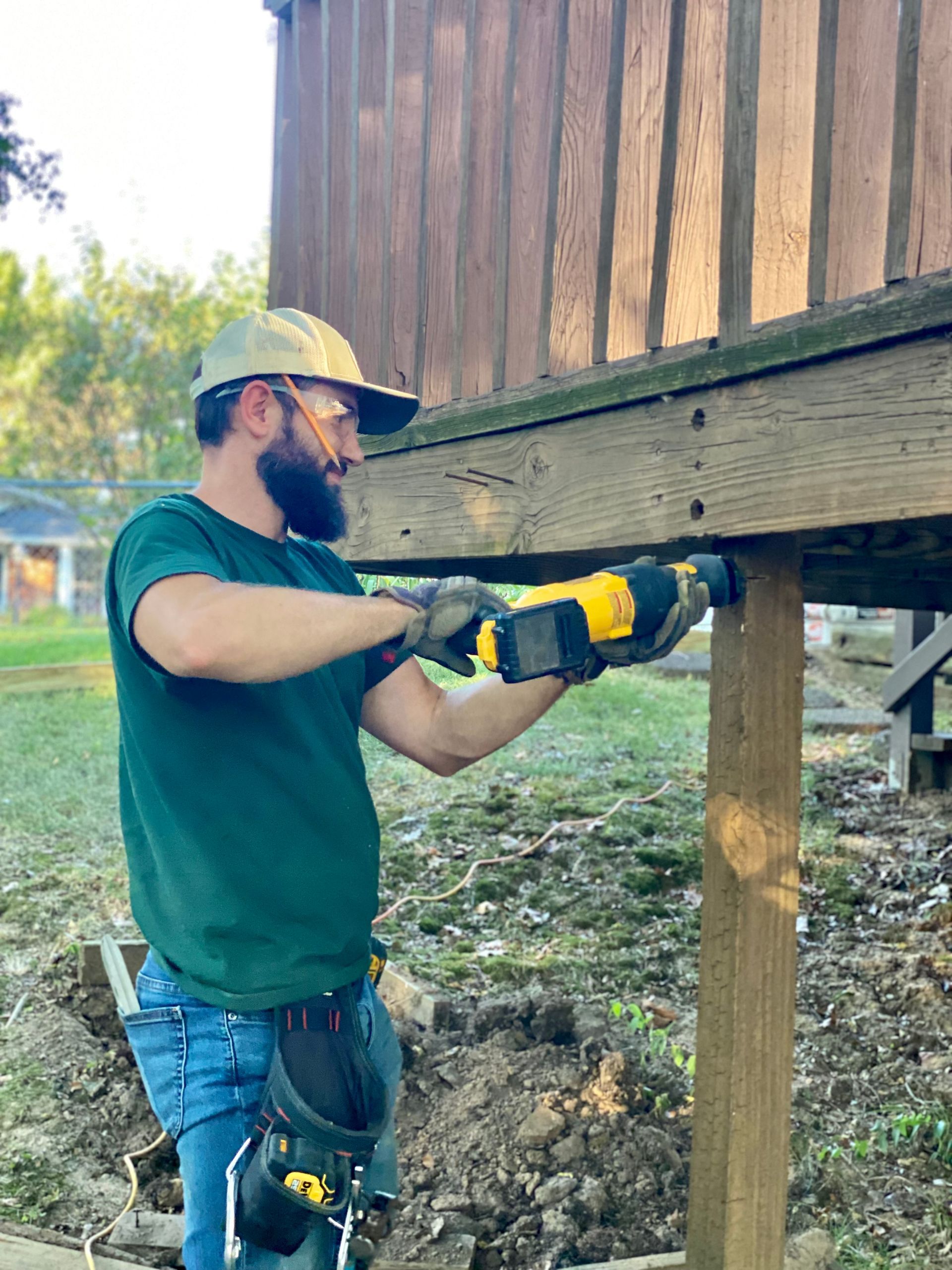 A man is working on a wooden deck with a drill.
