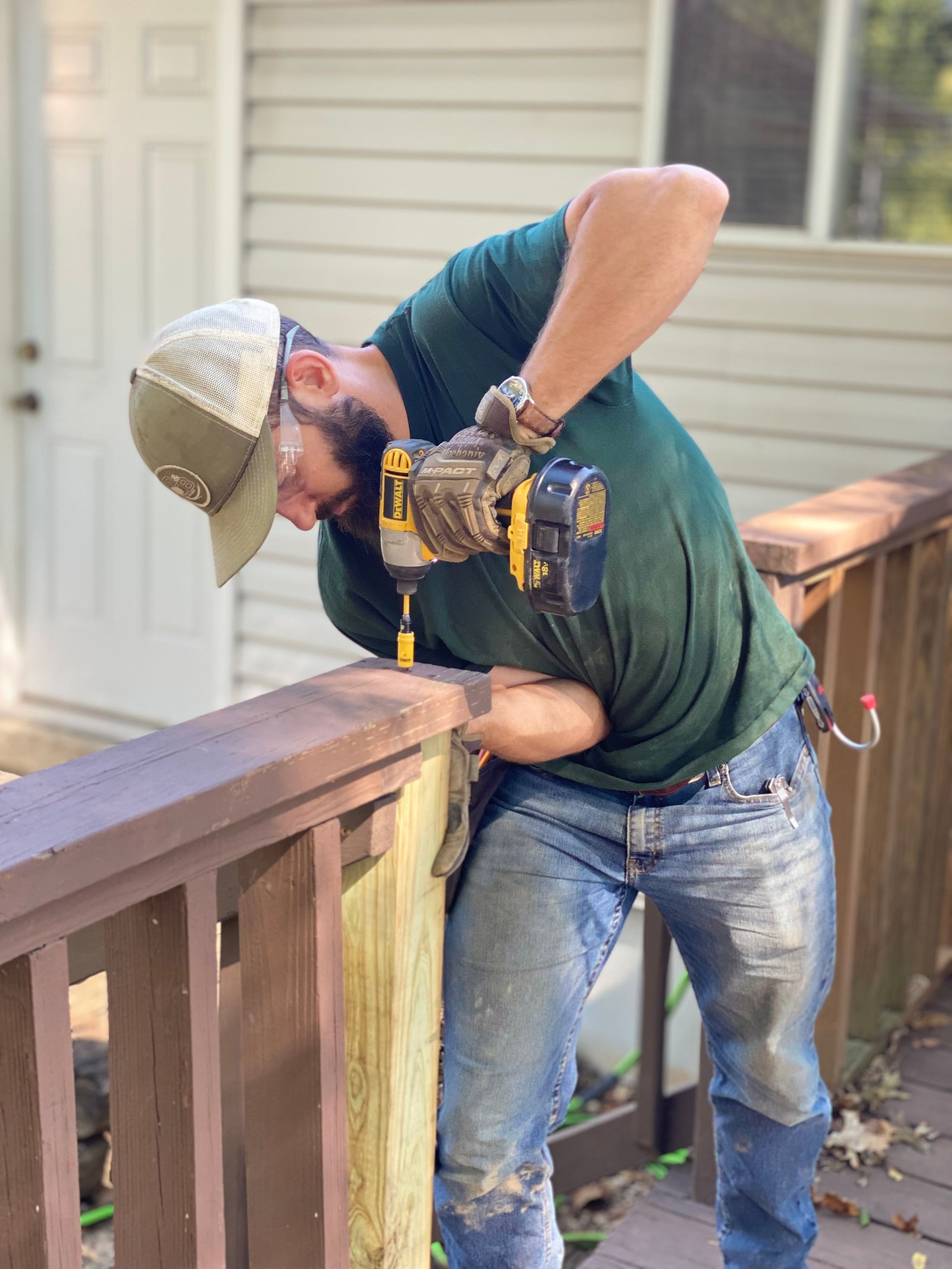 A man is using a drill to fix a wooden railing on a deck.