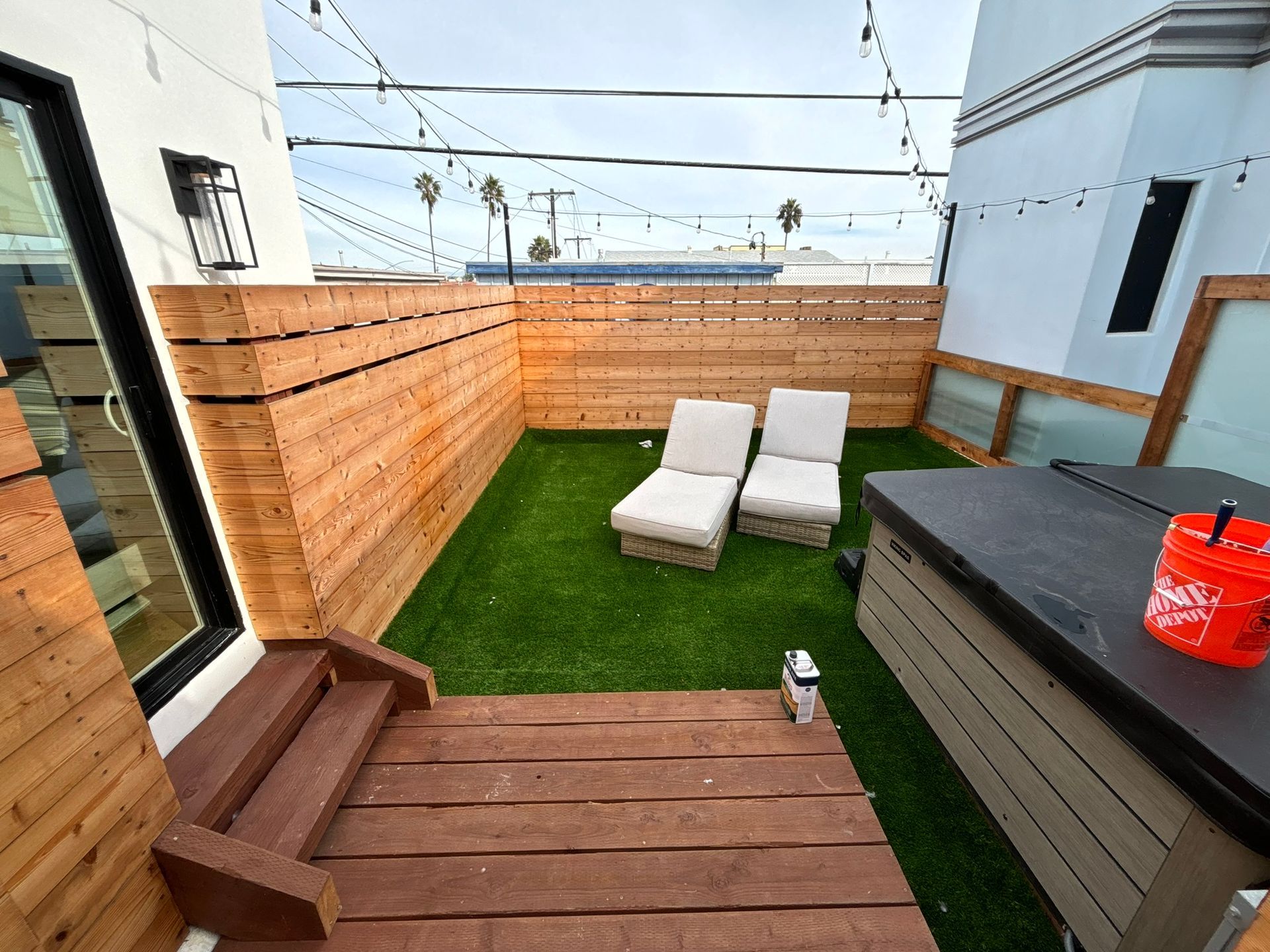 Wooden deck and artificial grass patio with lounge chairs and a hot tub.