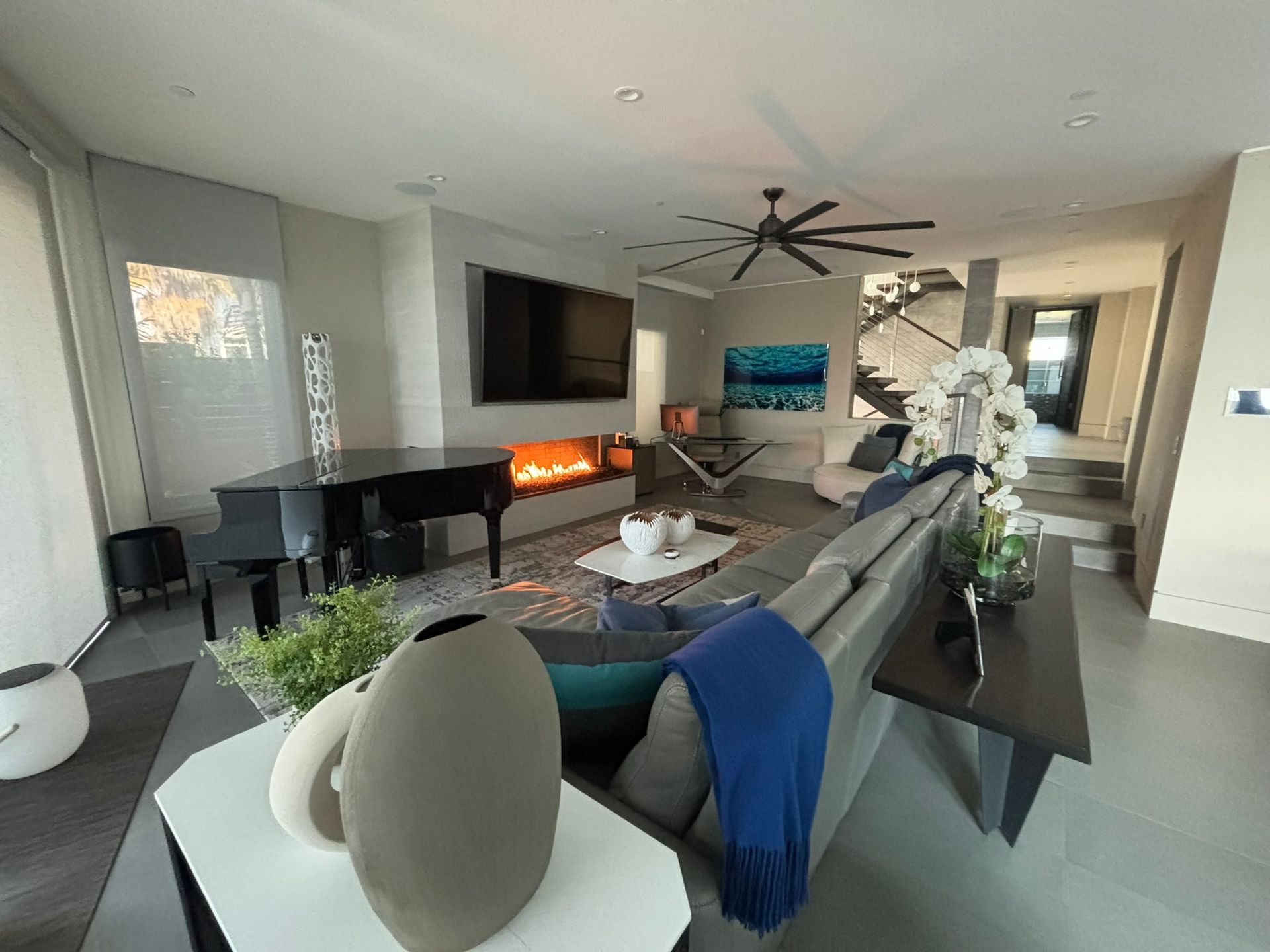 Modern living room with grand piano, fireplace, large TV, and sectional sofa.