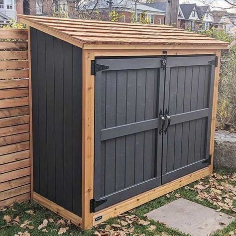 A wooden shed with black doors is sitting in the grass next to a wooden fence.