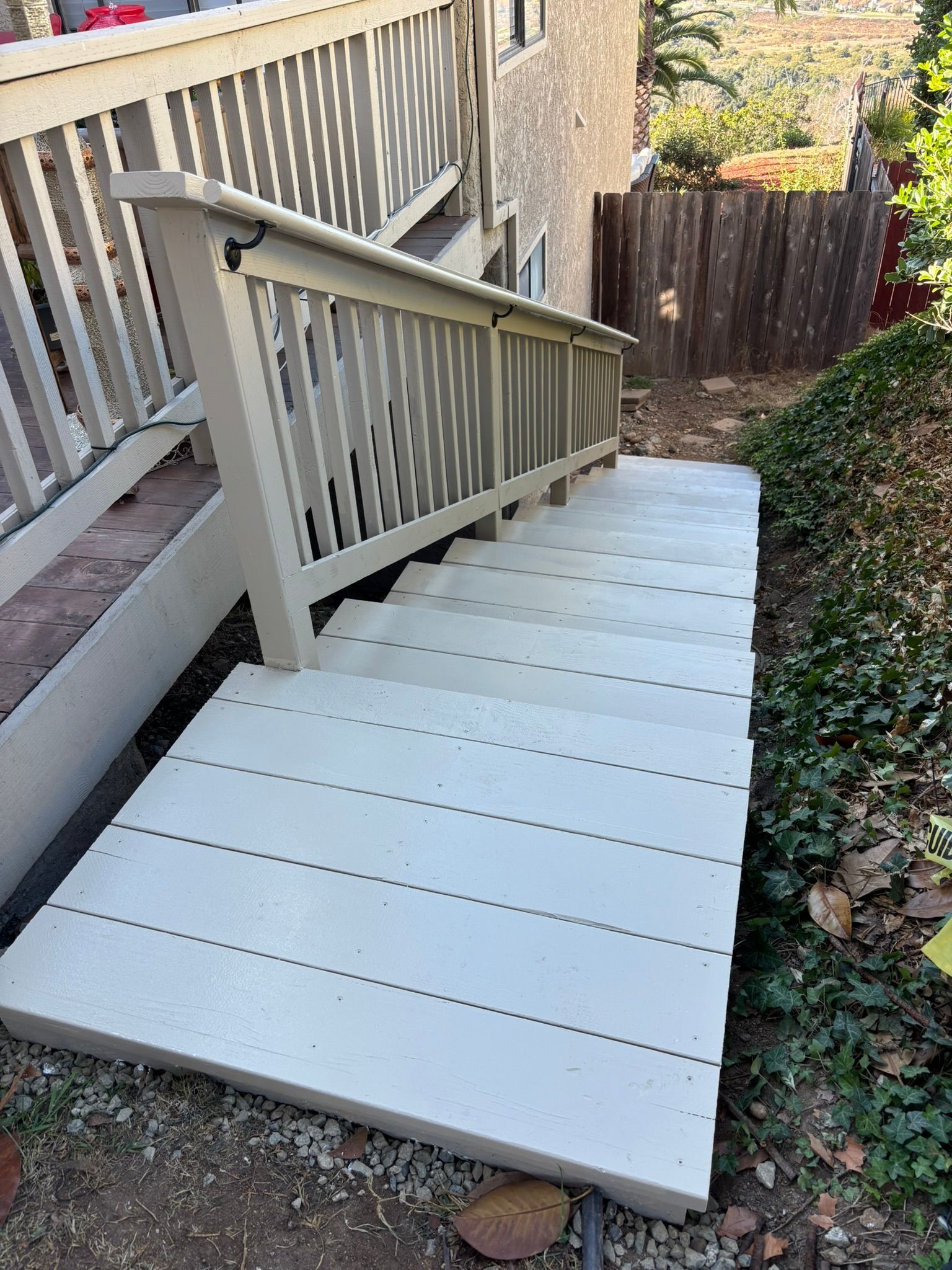 Outdoor staircase leading from a deck down to a yard, with light-colored steps and railing.