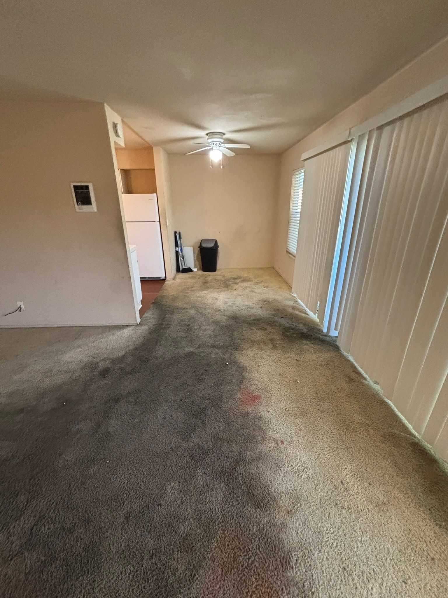 A living room with a carpeted floor and a ceiling fan.