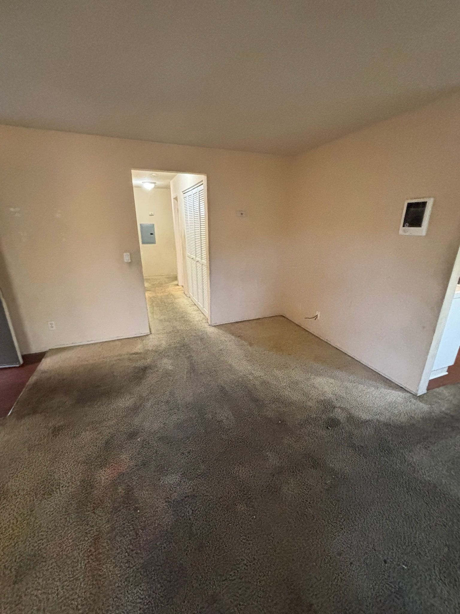 An empty living room with a carpeted floor and white walls.