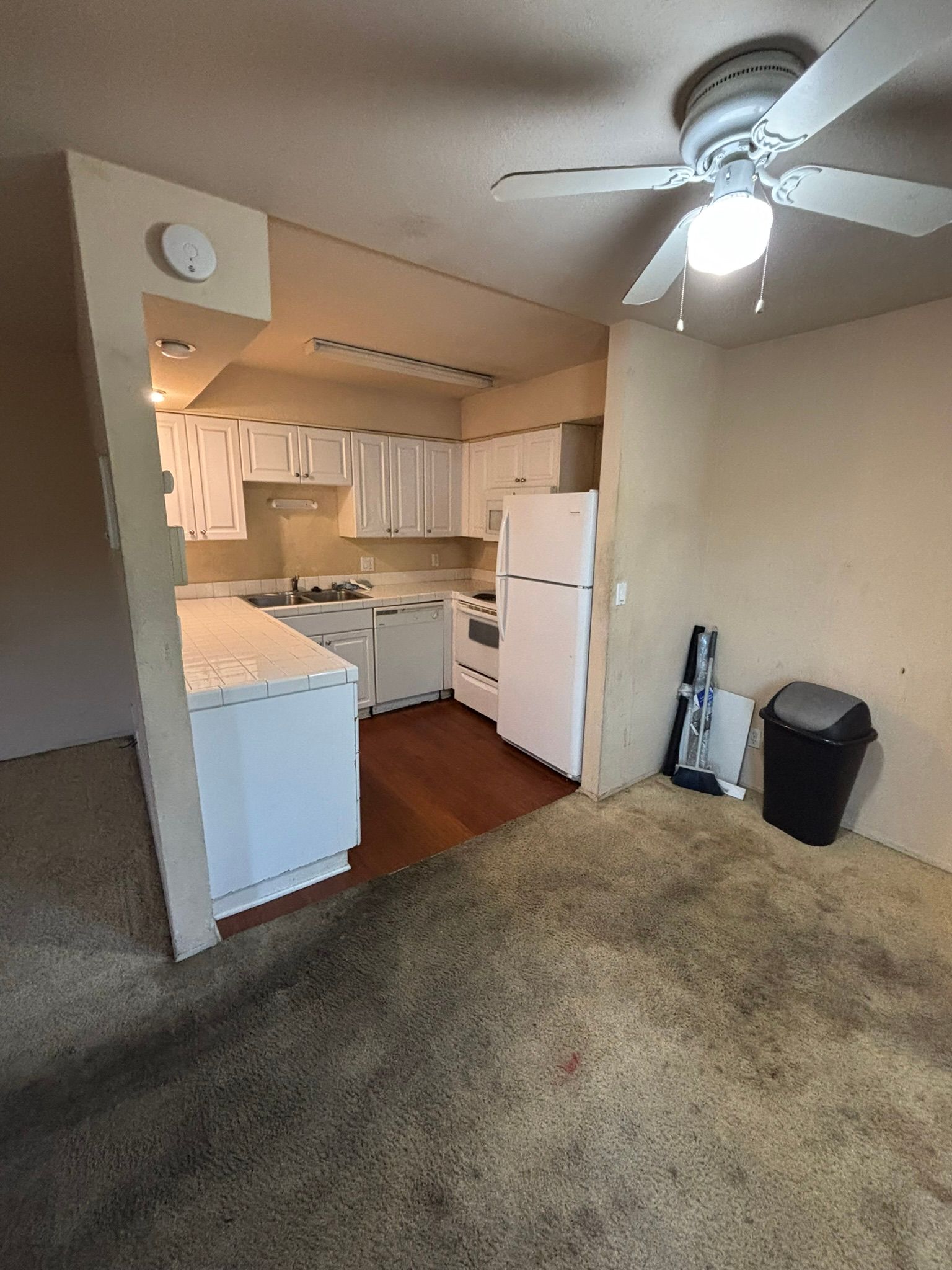 A kitchen with white cabinets , a refrigerator , and a ceiling fan.