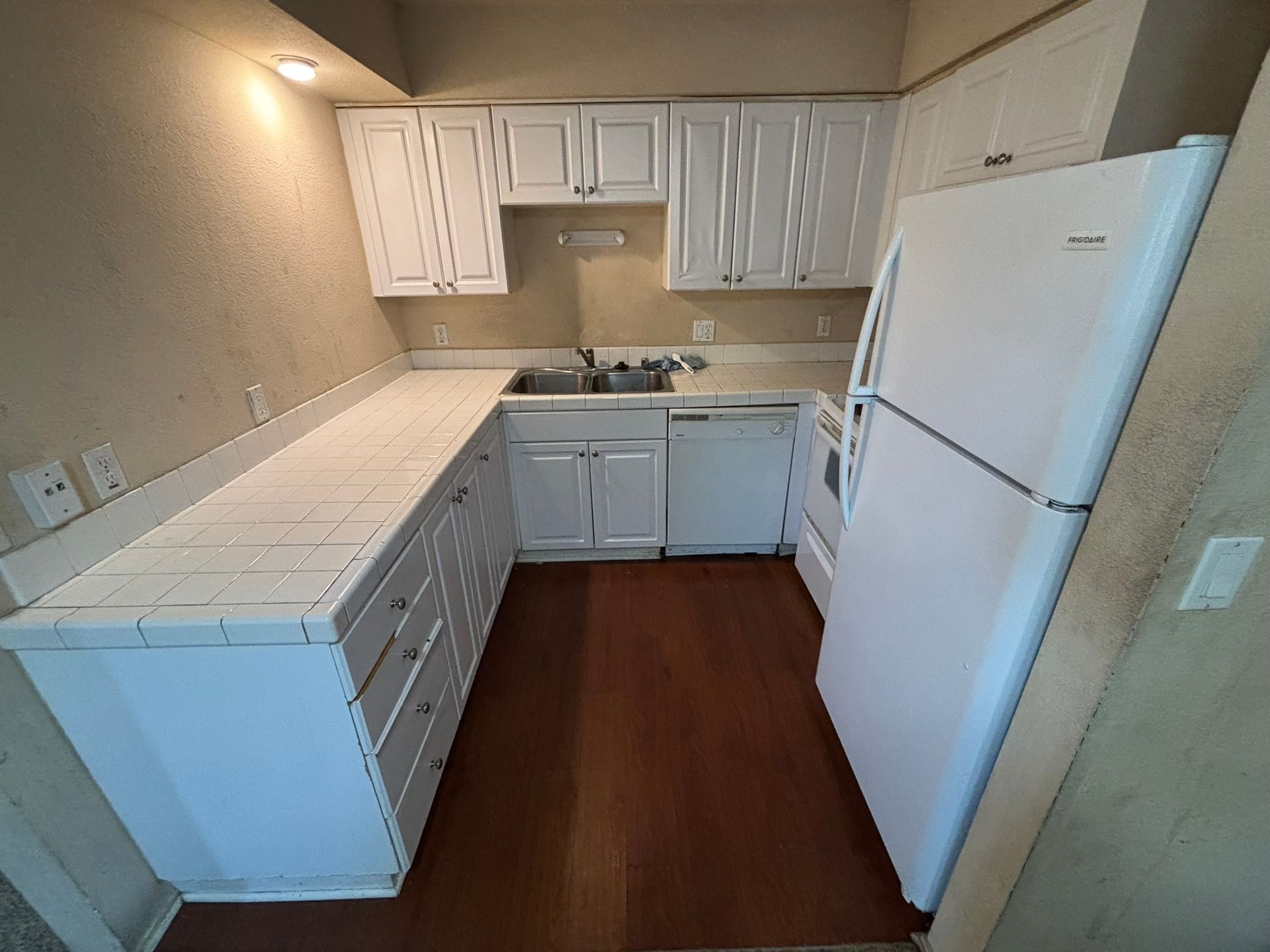 A kitchen with white cabinets , a refrigerator , a sink , and a dishwasher.