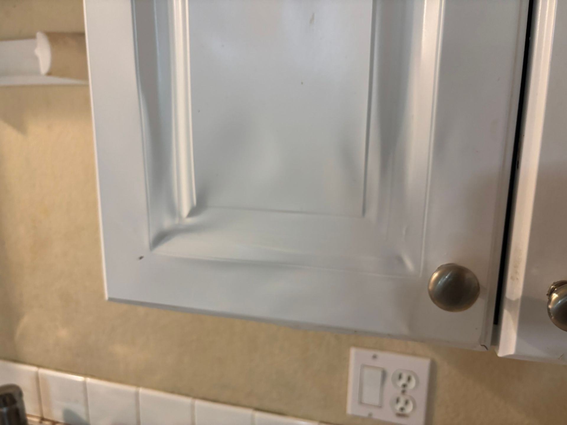 A kitchen with white cabinets and a white electrical outlet.