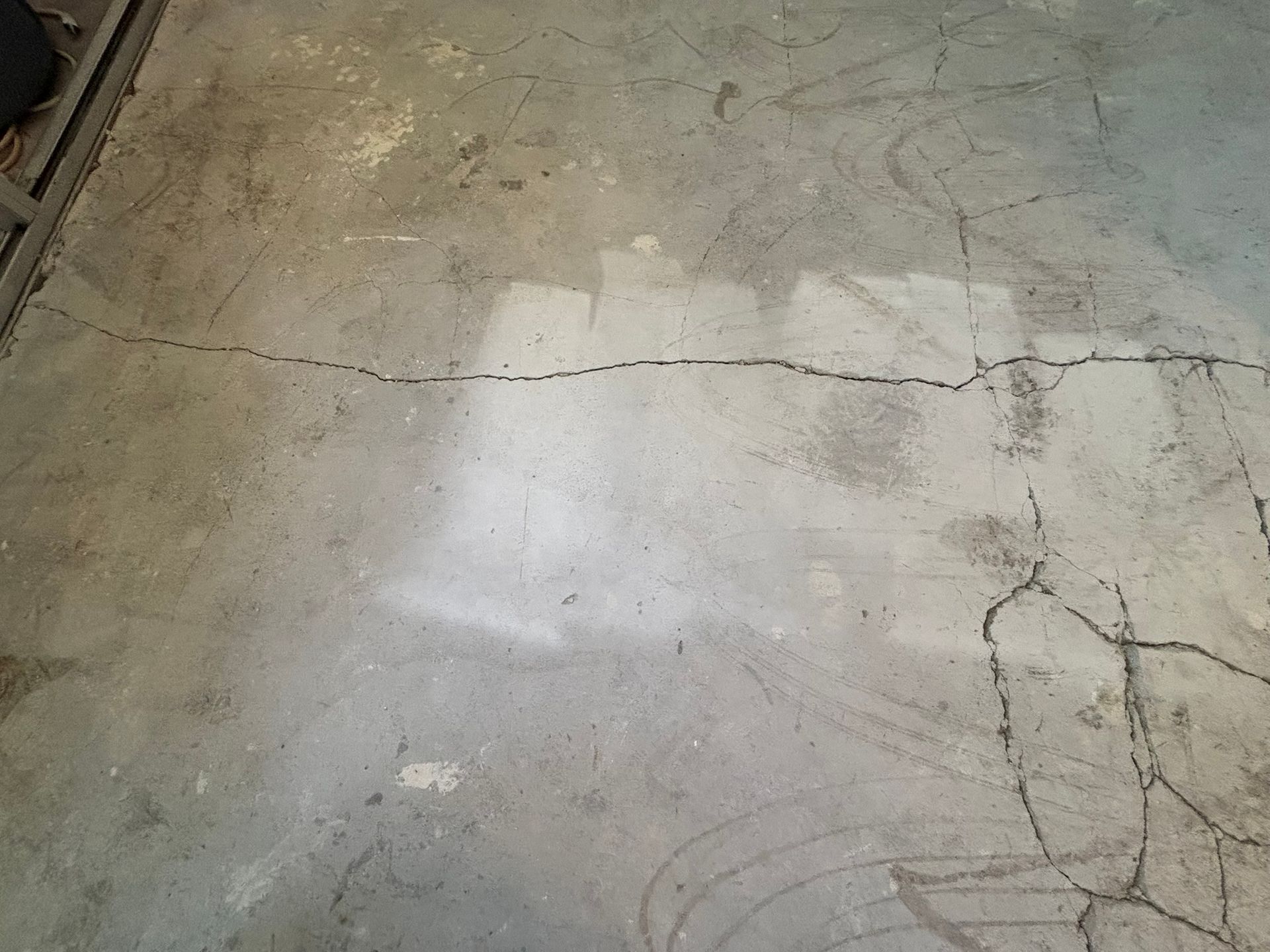 Cracked concrete floor with long horizontal and spiderweb-like cracks, in a garage or similar setting.