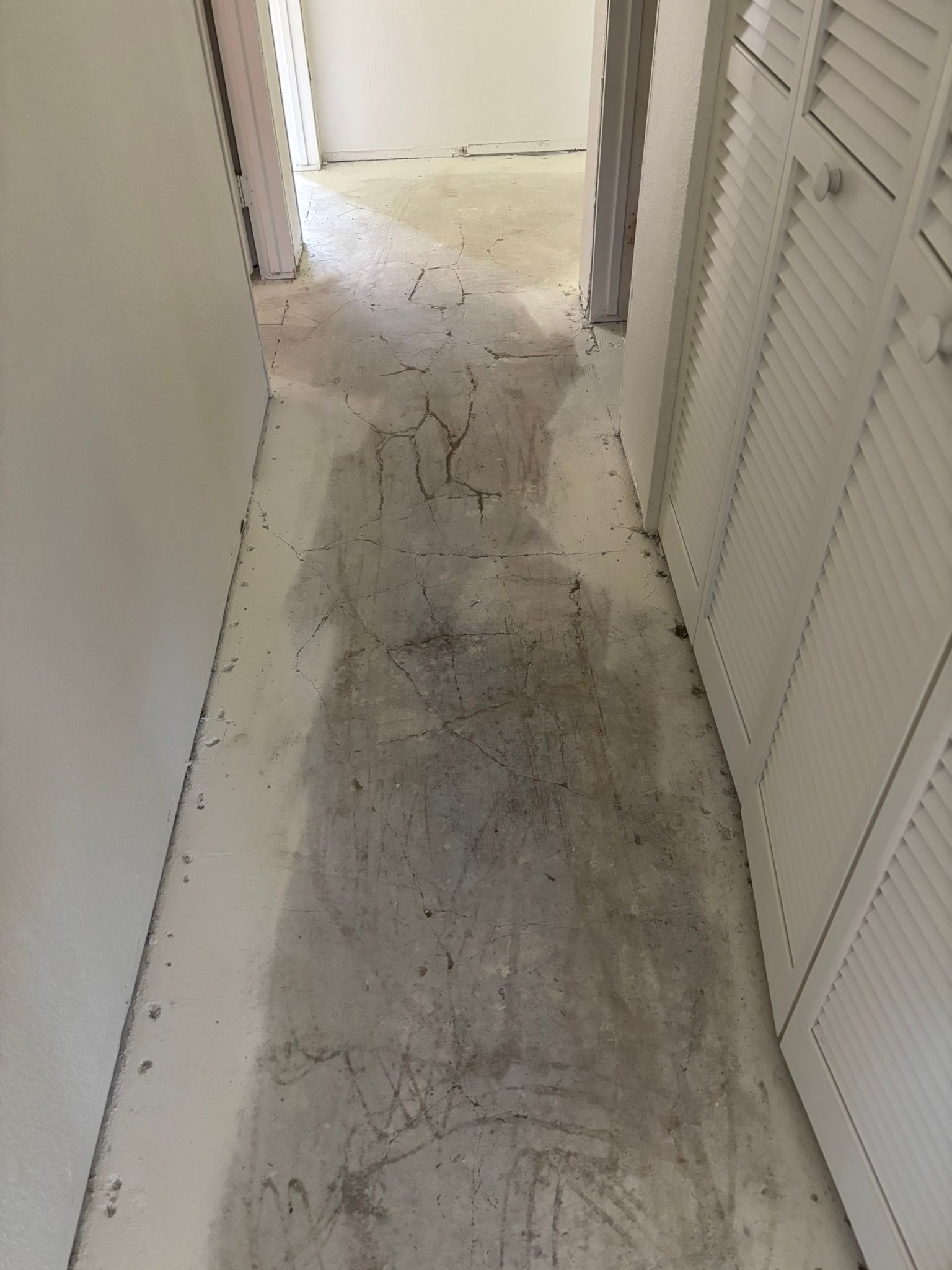 A hallway with a dirty floor and white cabinets.