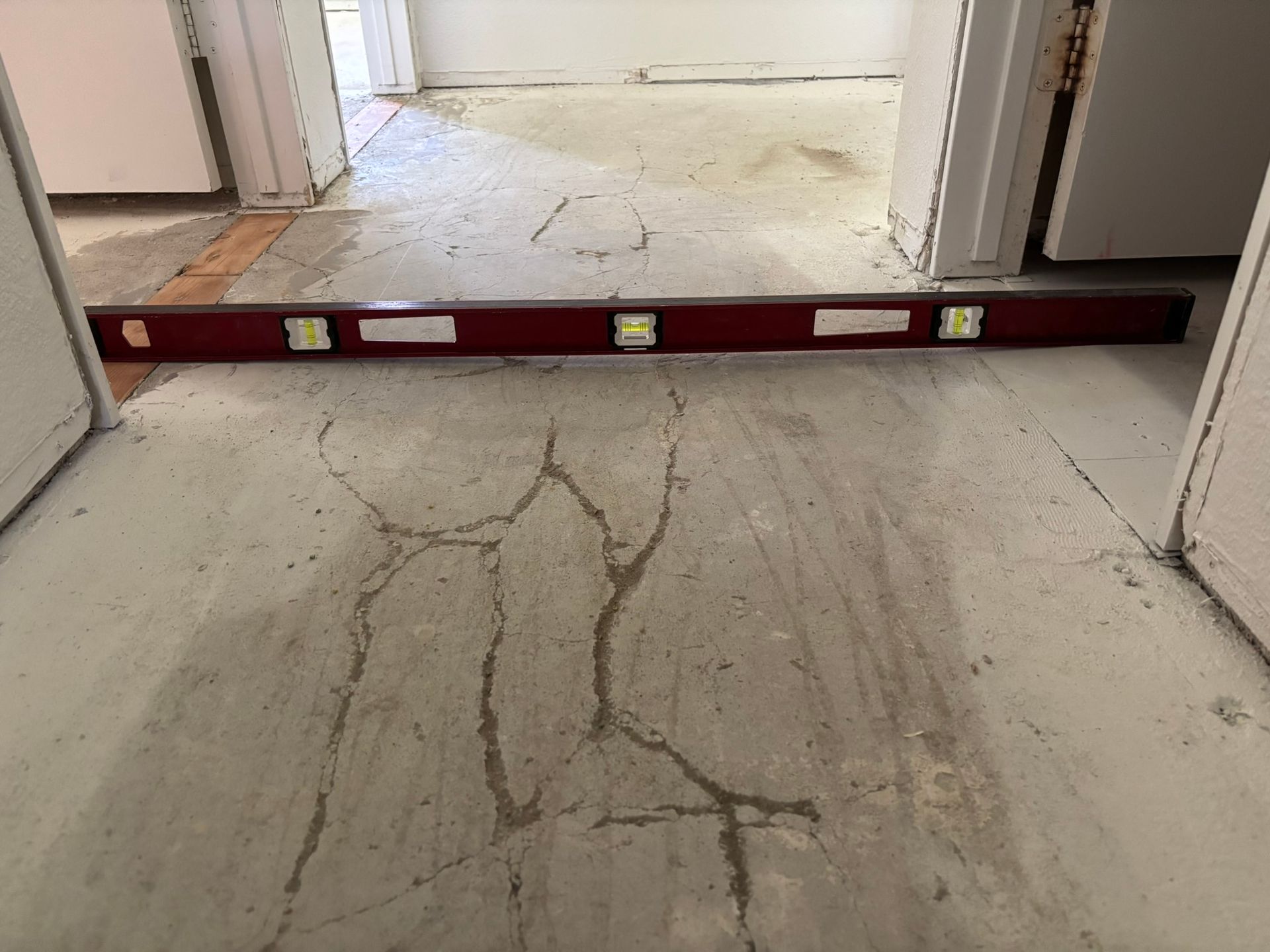 Level on a cracked concrete floor in a doorway, indicating unevenness.
