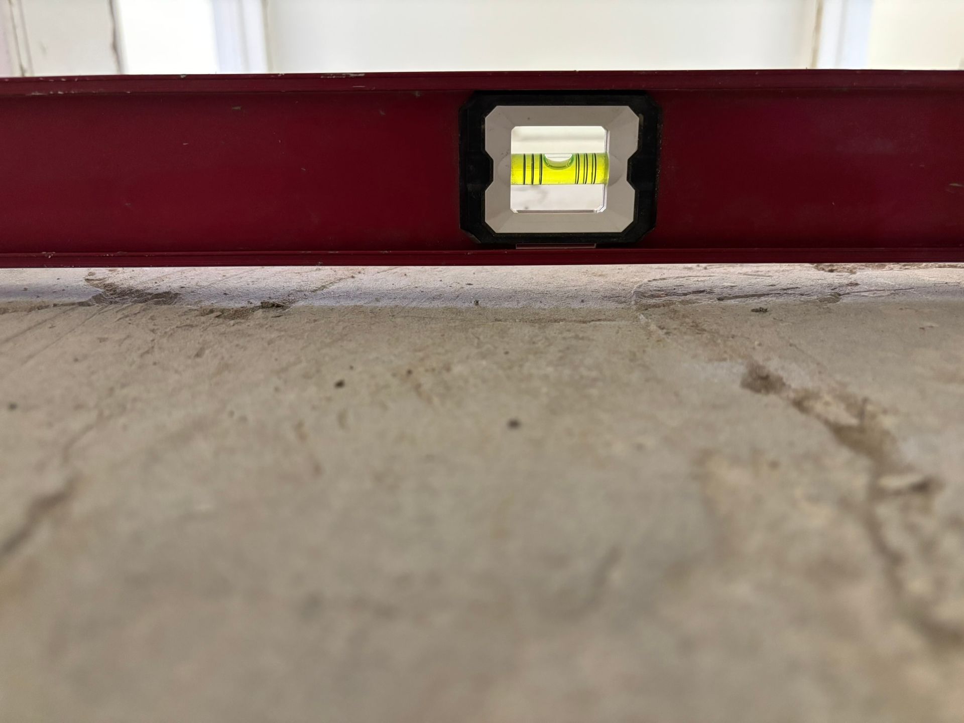 A red level is sitting on a concrete floor.