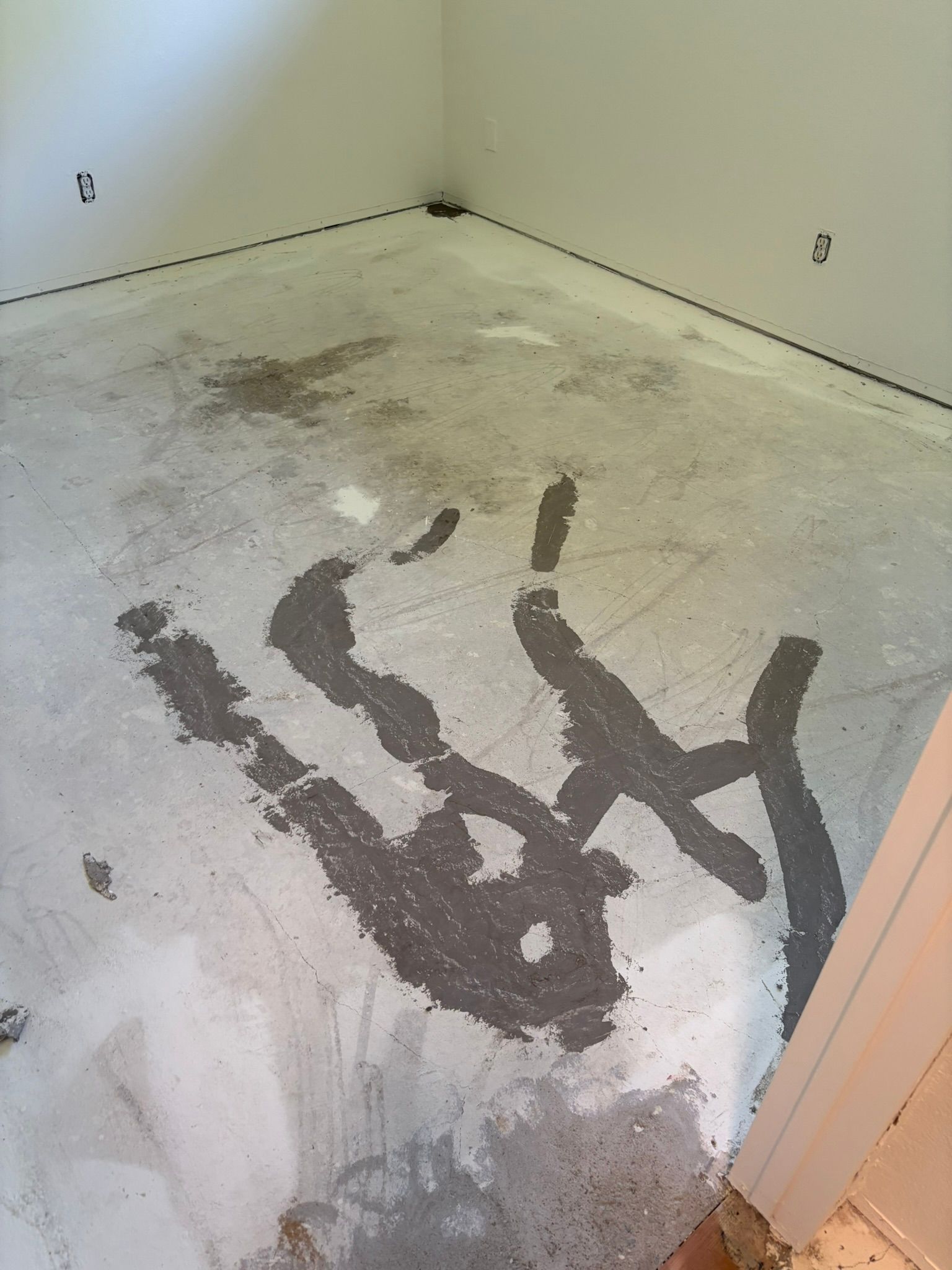Gray handprint-shaped splotch on a concrete floor in a room with white walls and unfinished edges.