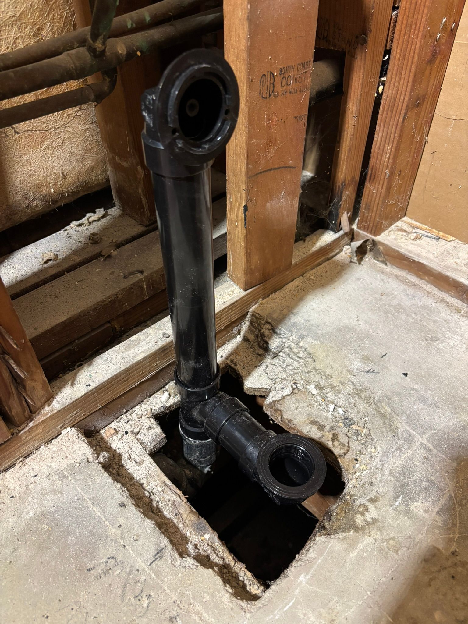 A black pipe is sitting in a hole in a wall.