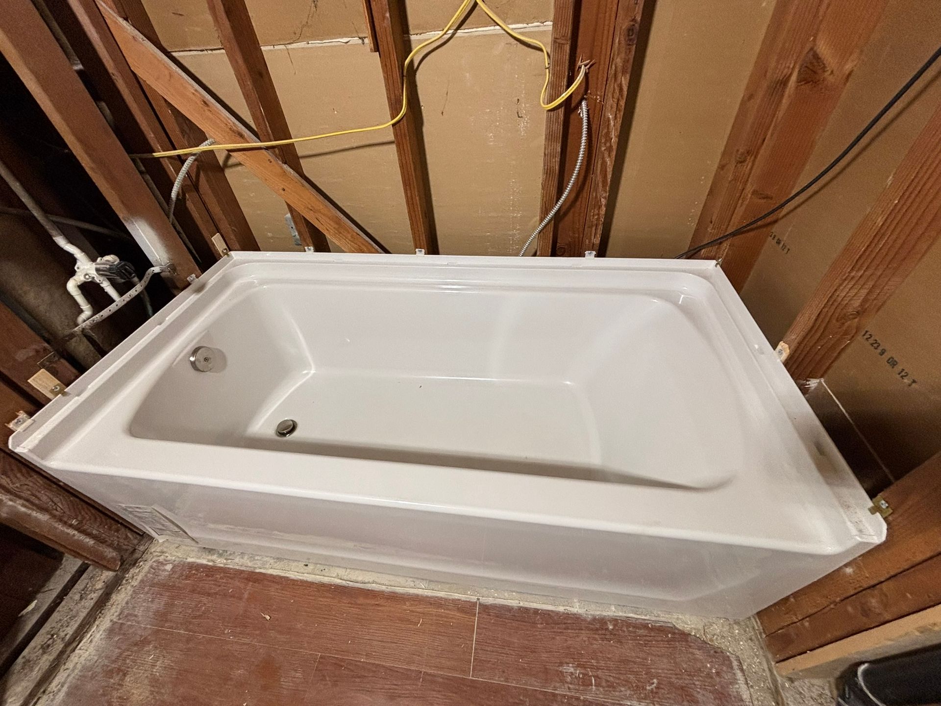A white bathtub is sitting in a bathroom under construction.
