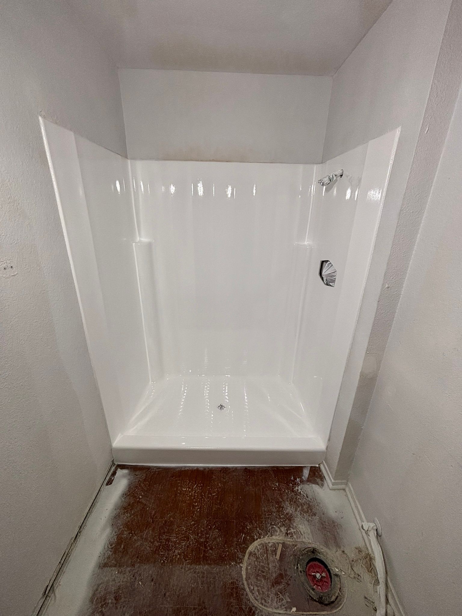 White shower stall installed in a small bathroom. The floor is unfinished with debris.