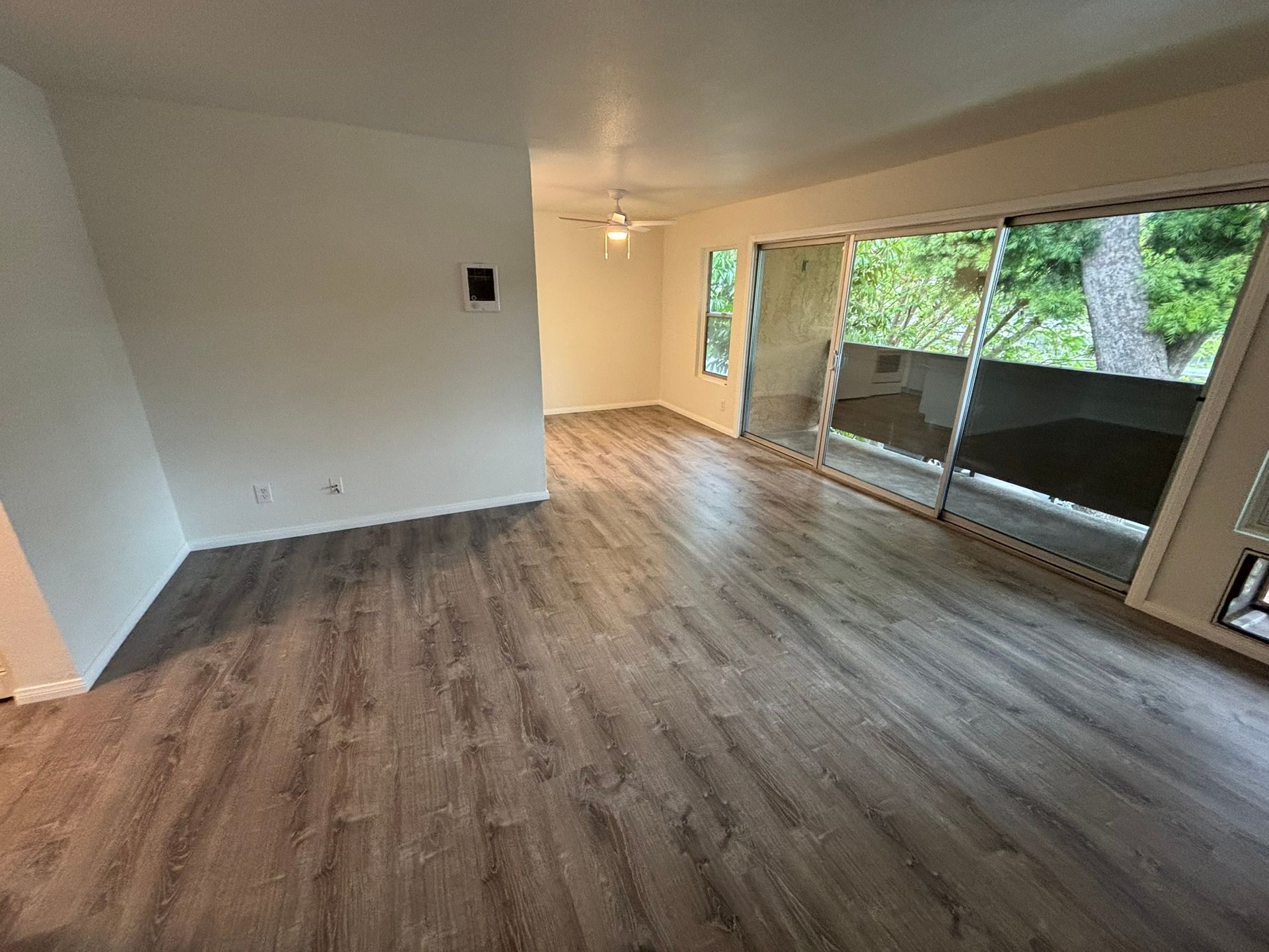 An empty living room with hardwood floors and sliding glass doors.