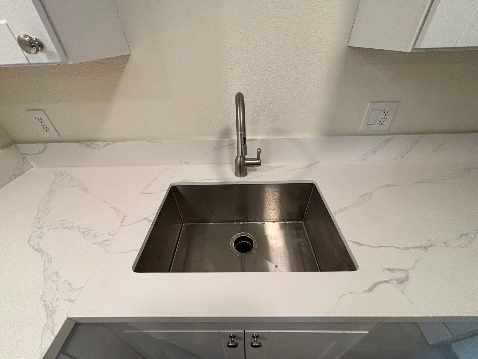 A kitchen sink with a stainless steel faucet on a marble counter top.