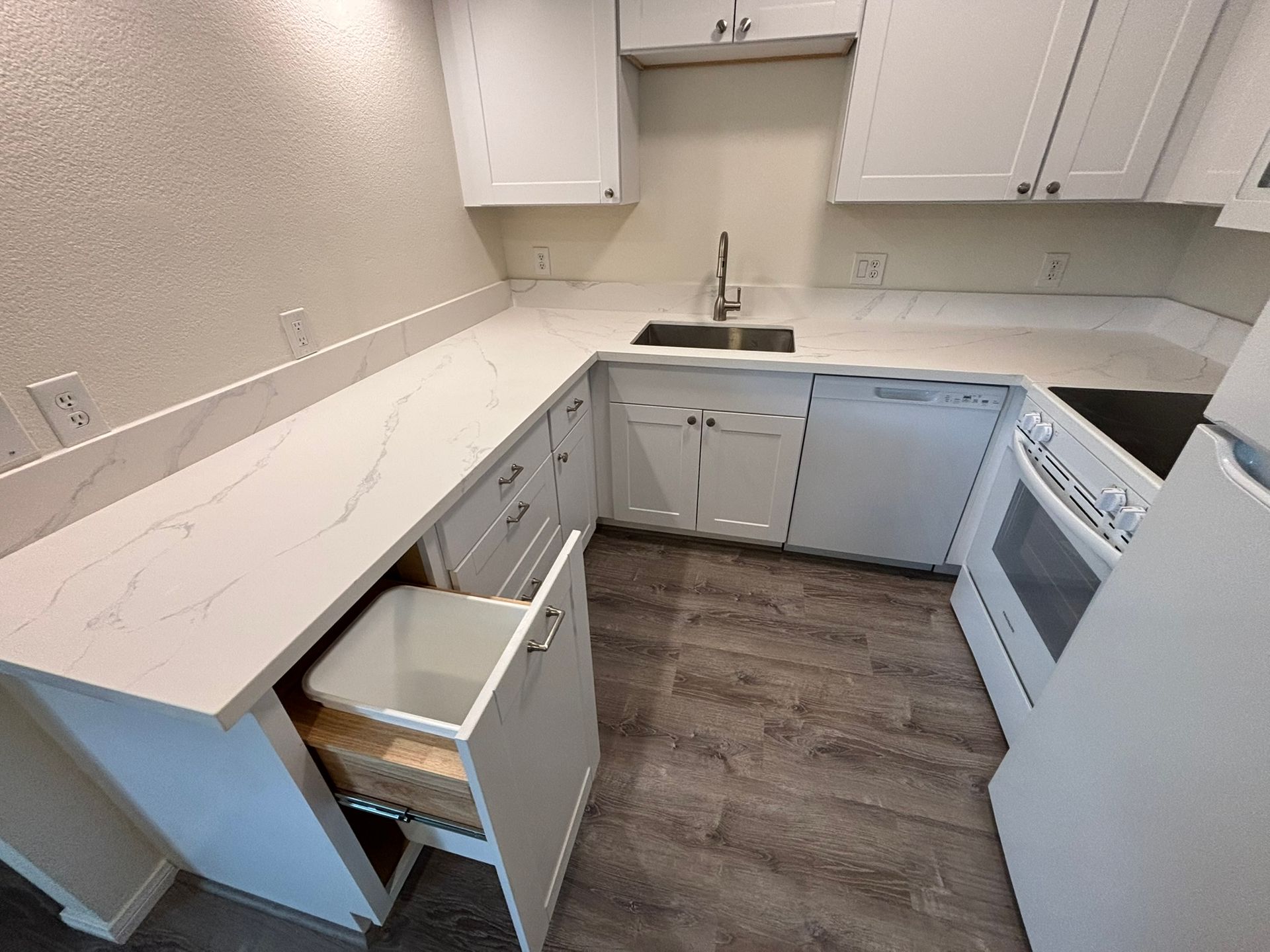 A kitchen with white cabinets , a sink , a refrigerator , and a trash can.