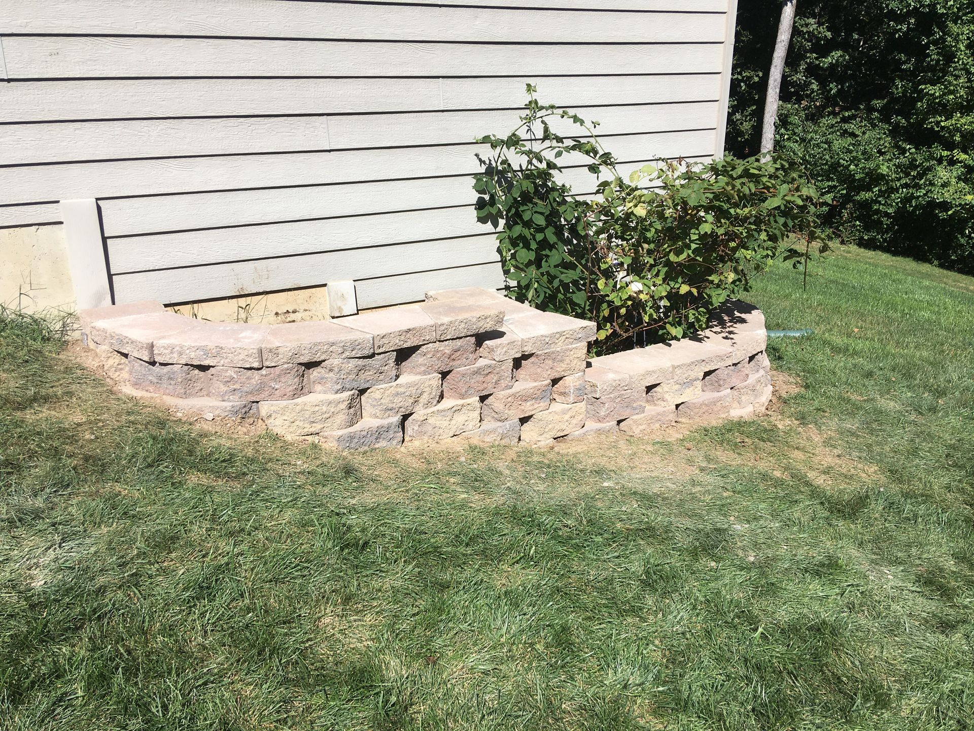 A stone wall is sitting in the grass in front of a house.