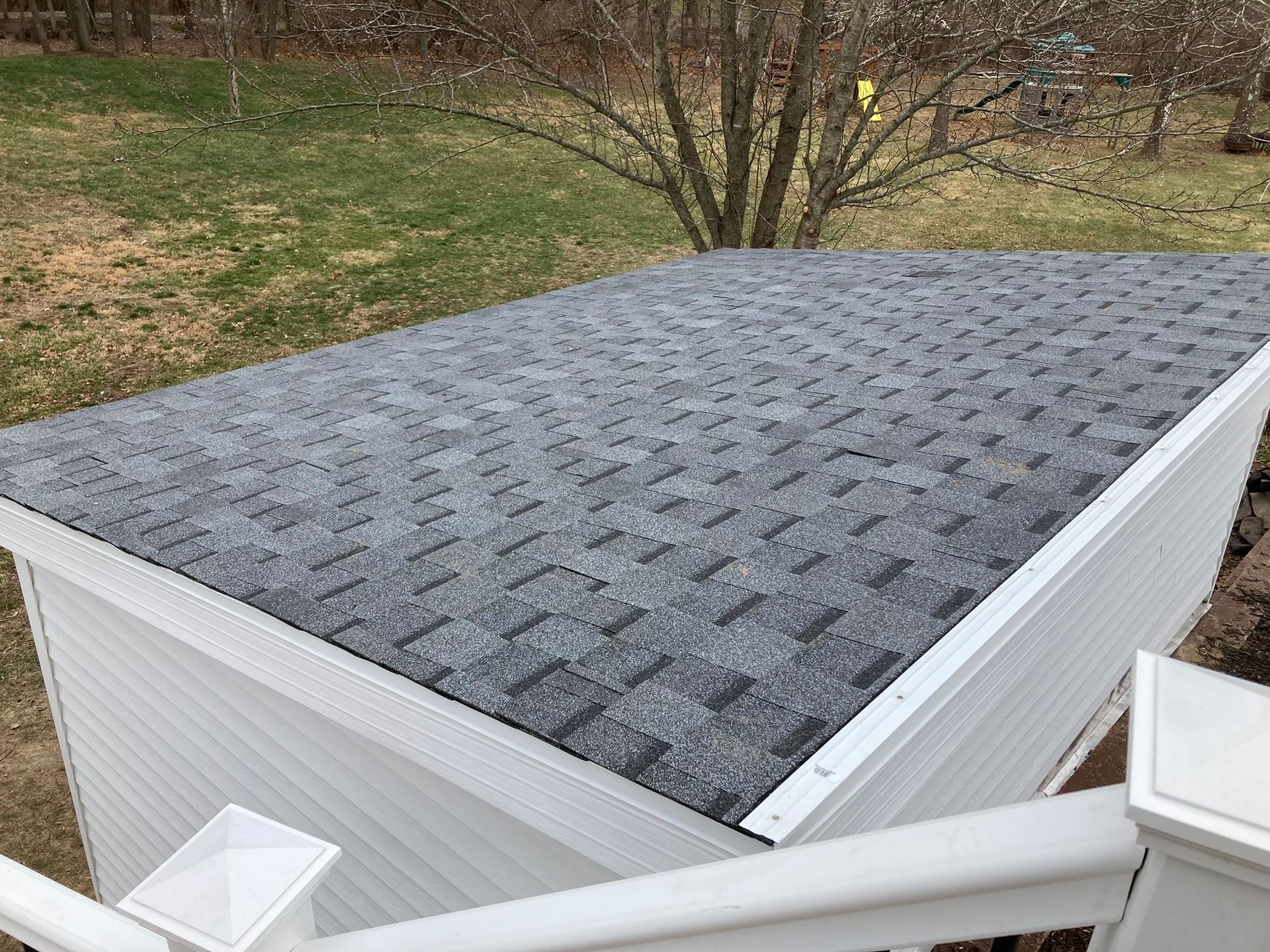 Gray shingle roof on a white shed, viewed from above, with a green yard in the background.