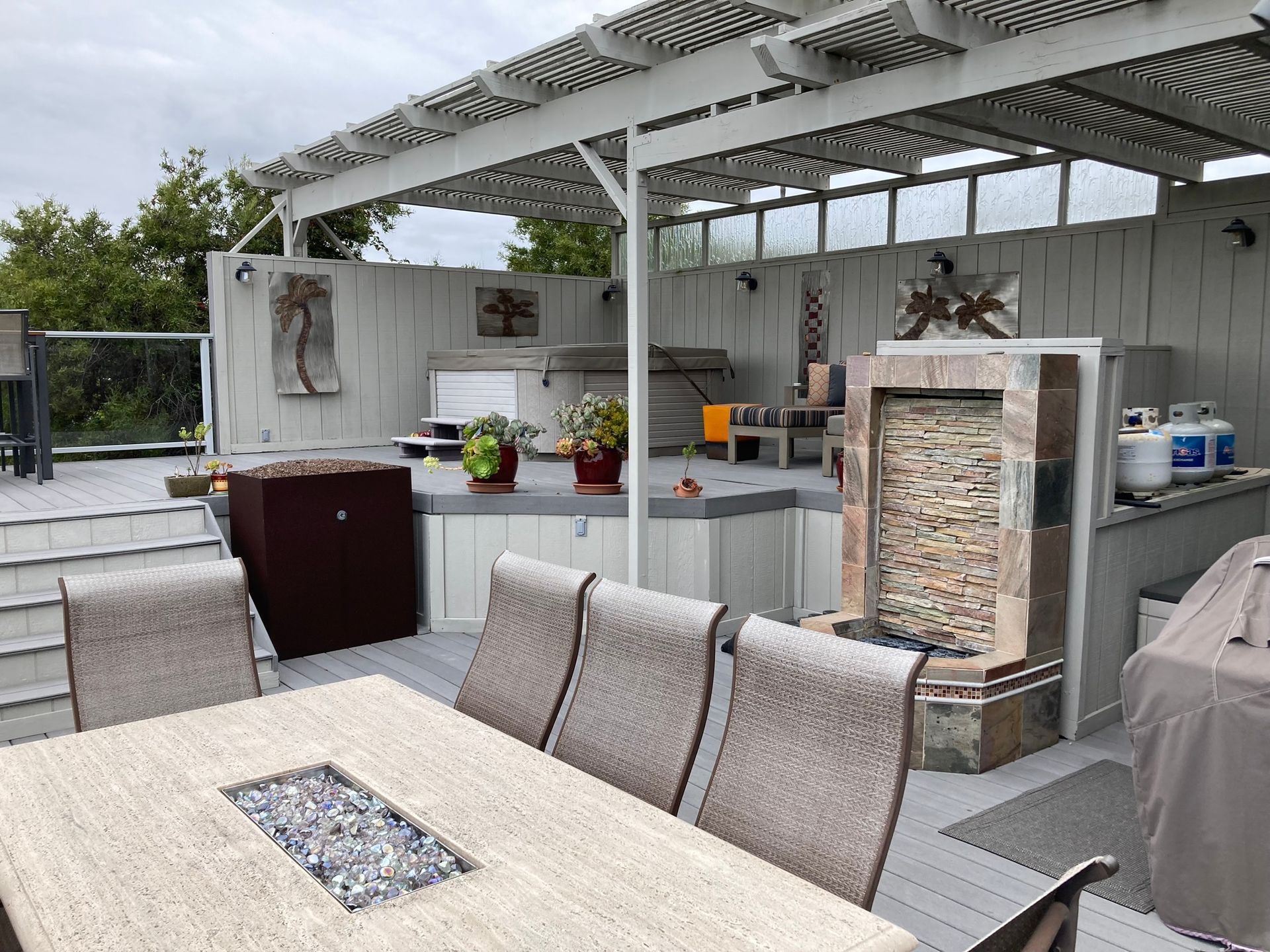Outdoor deck with dining table, fireplace, and hot tub under a pergola.