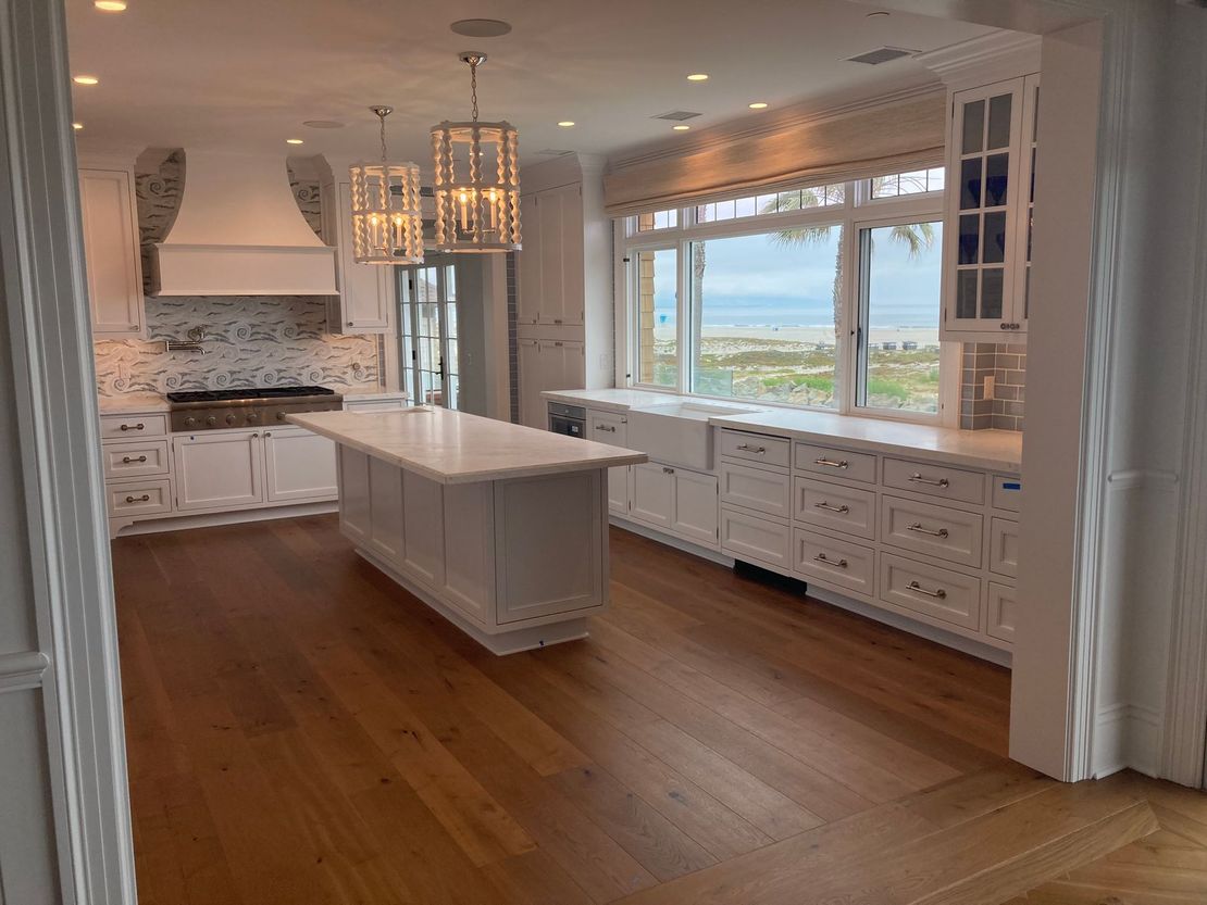 A large kitchen with white cabinets , hardwood floors , and a large island.
