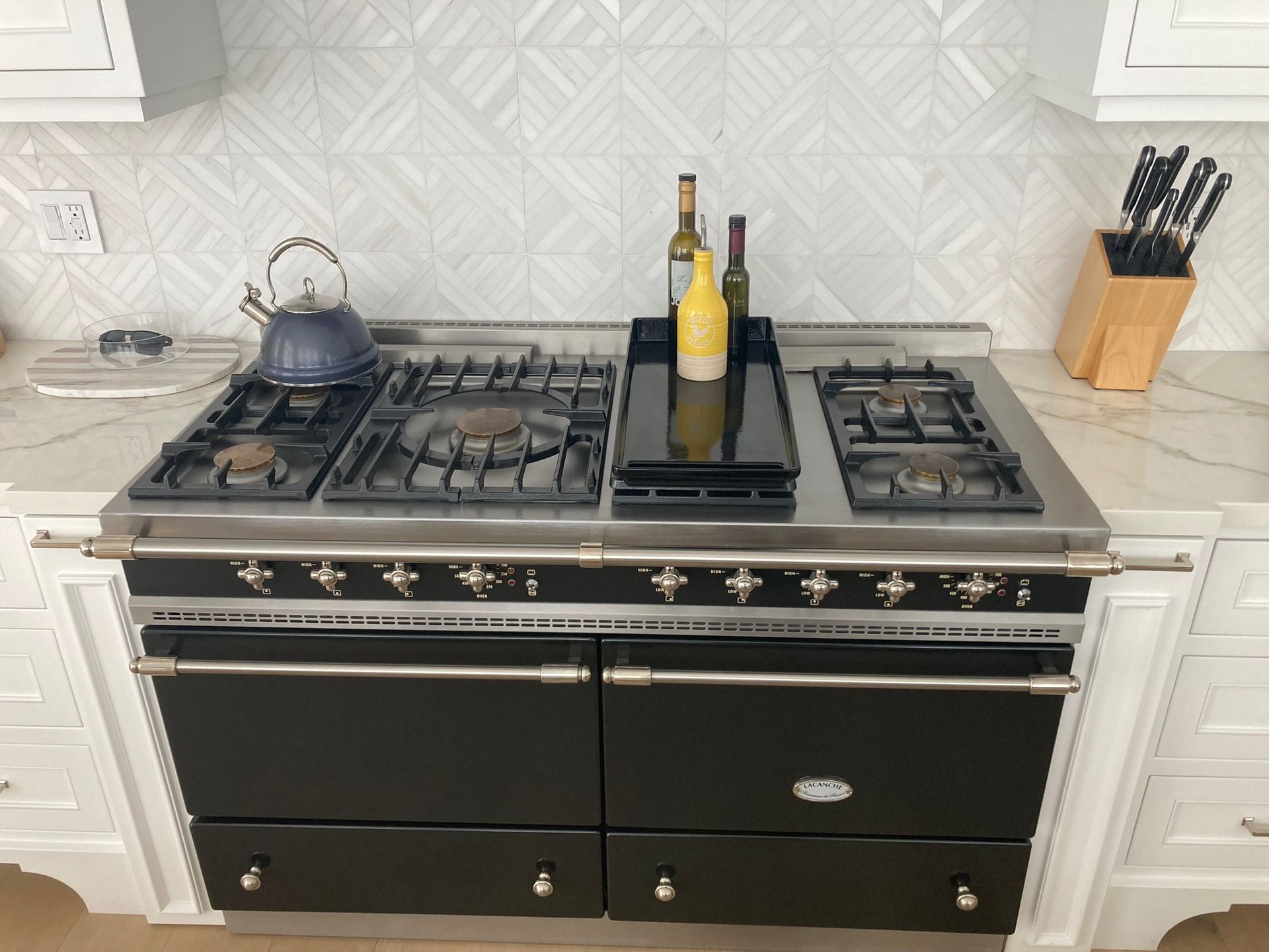 Black and stainless steel range in a white kitchen with cookware and bottles on the stovetop.