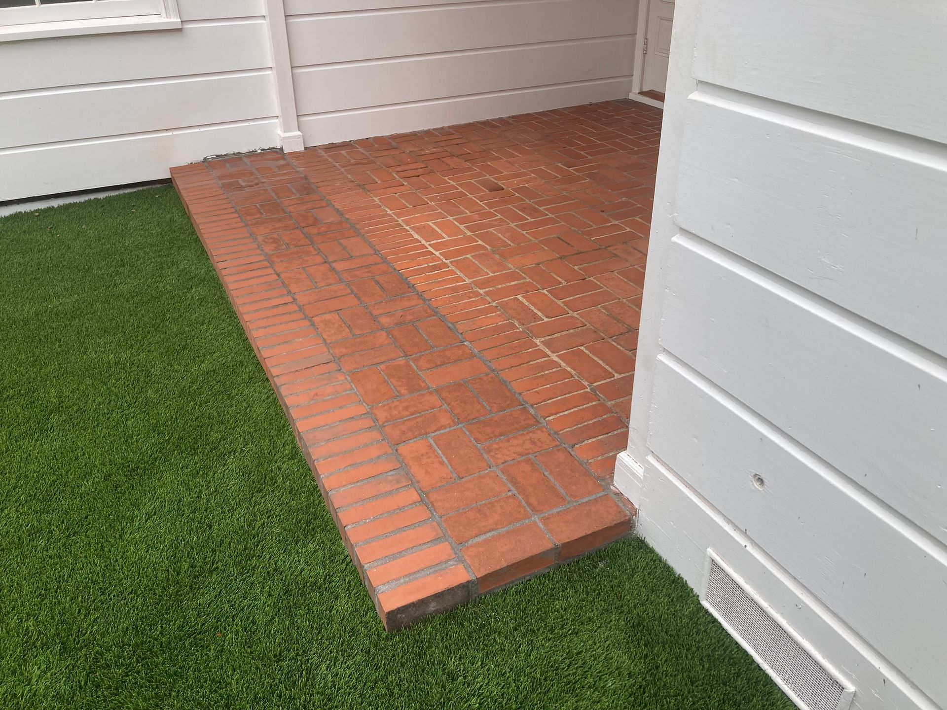 A brick patio with a green lawn in front of a white house.