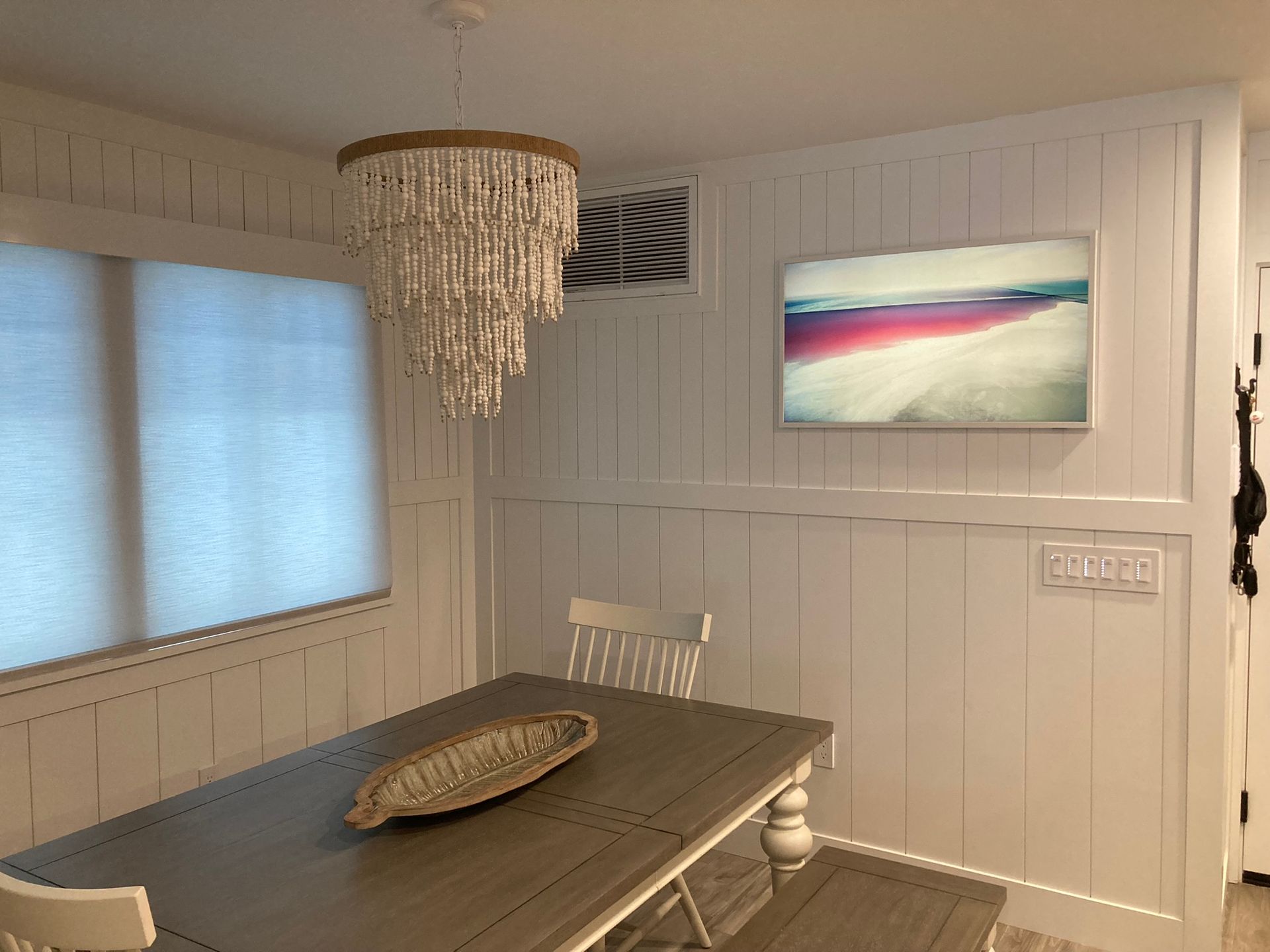 A dining room with a table and chairs and a picture on the wall.