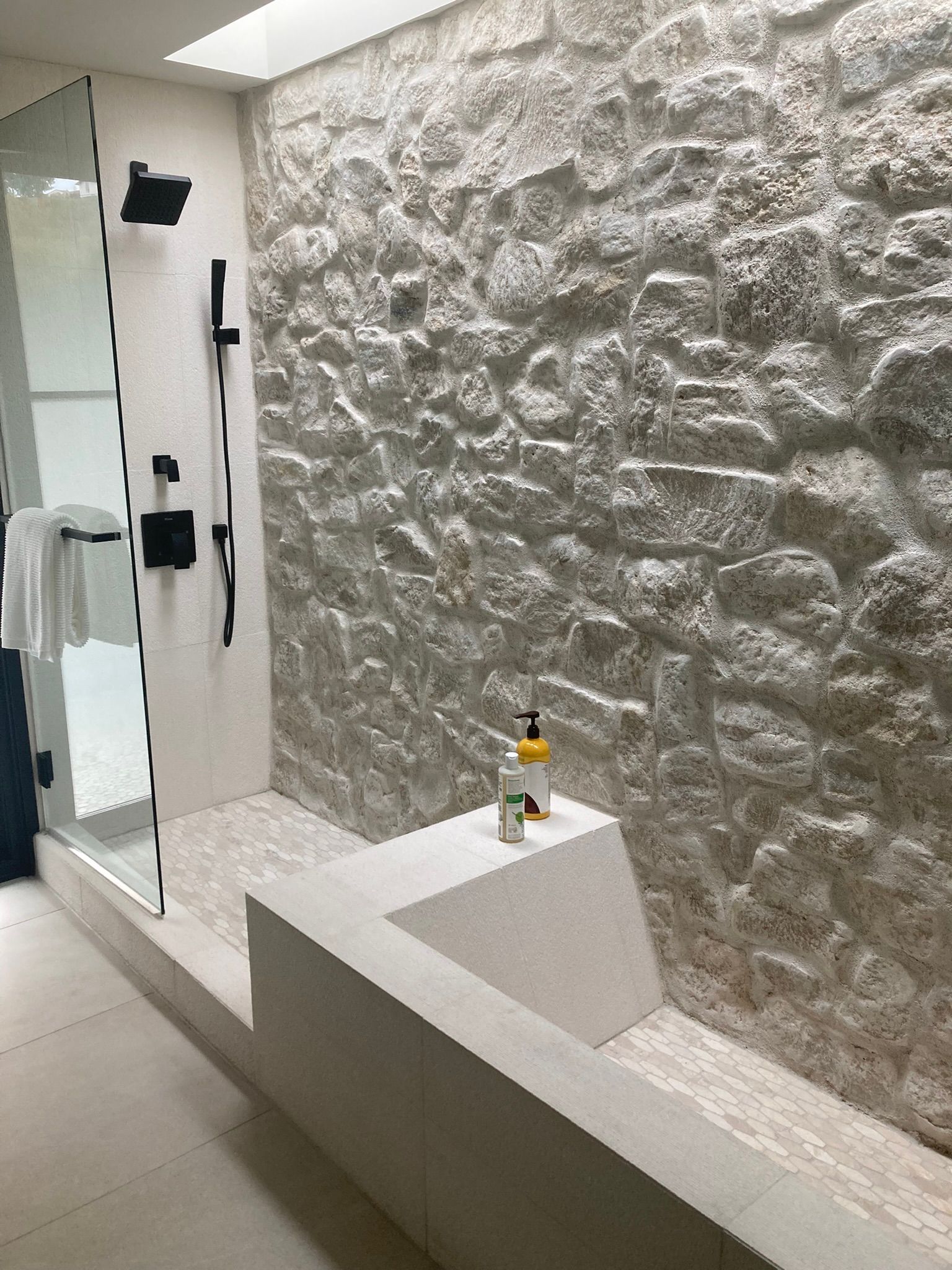 Stone-walled shower with black fixtures and a built-in bench. The shower floor is stone.