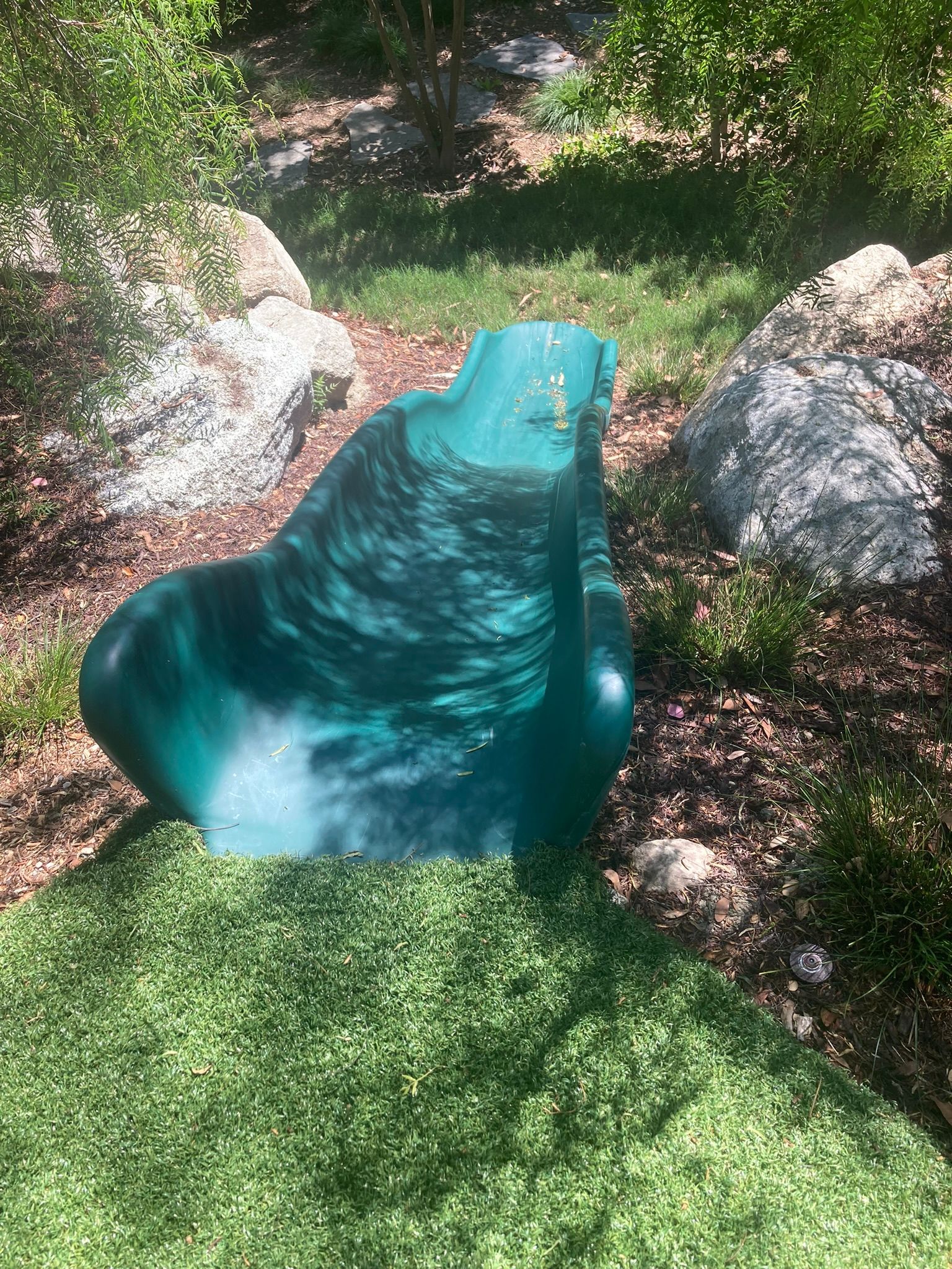 A green slide is sitting on top of a lush green lawn.