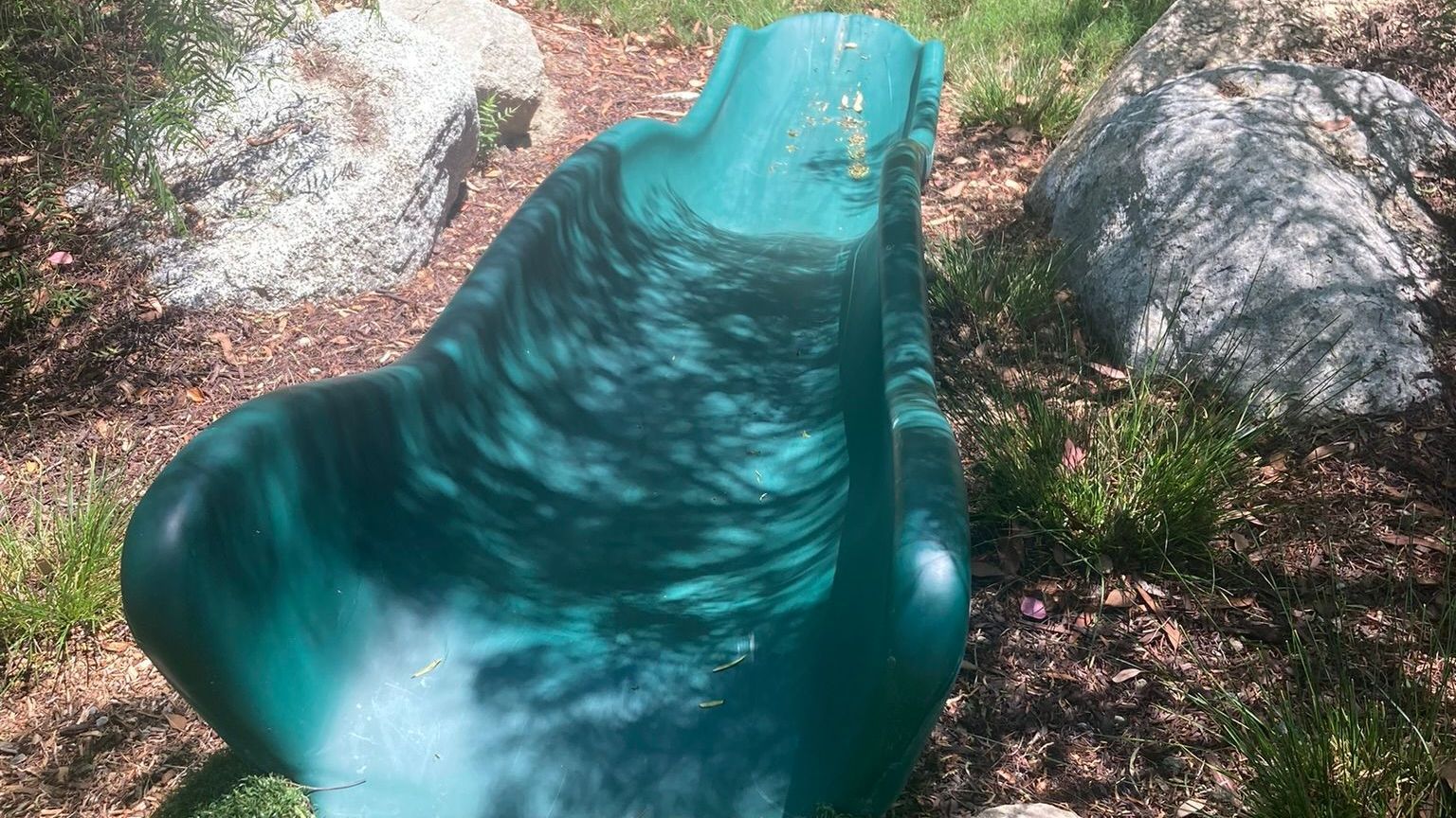 A green chair is sitting in the grass next to rocks.