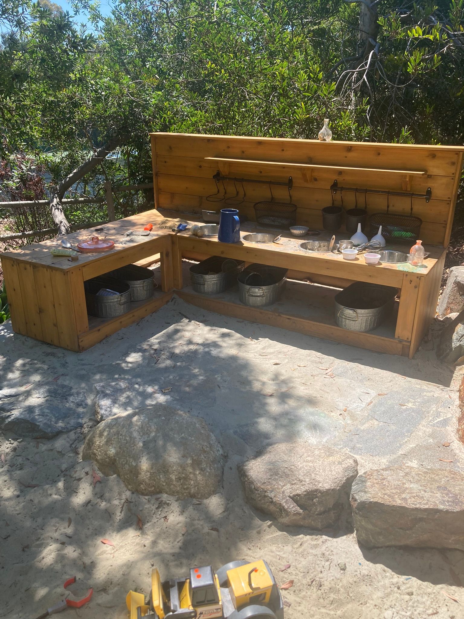 A wooden table with pots and pans on it is sitting on top of a sandy area.