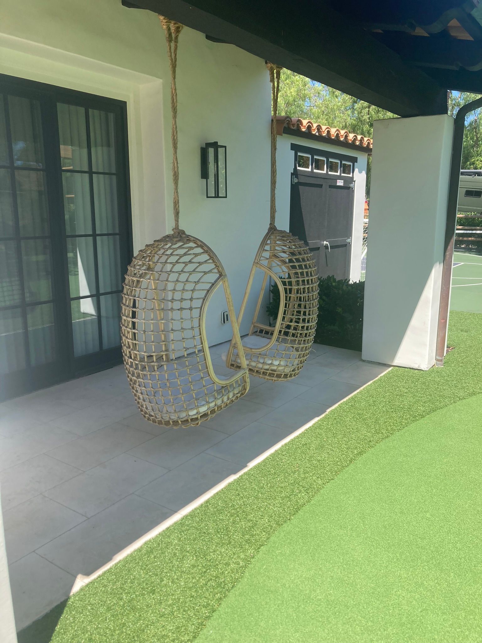 Two wicker hanging chairs are hanging from a rope on a patio.