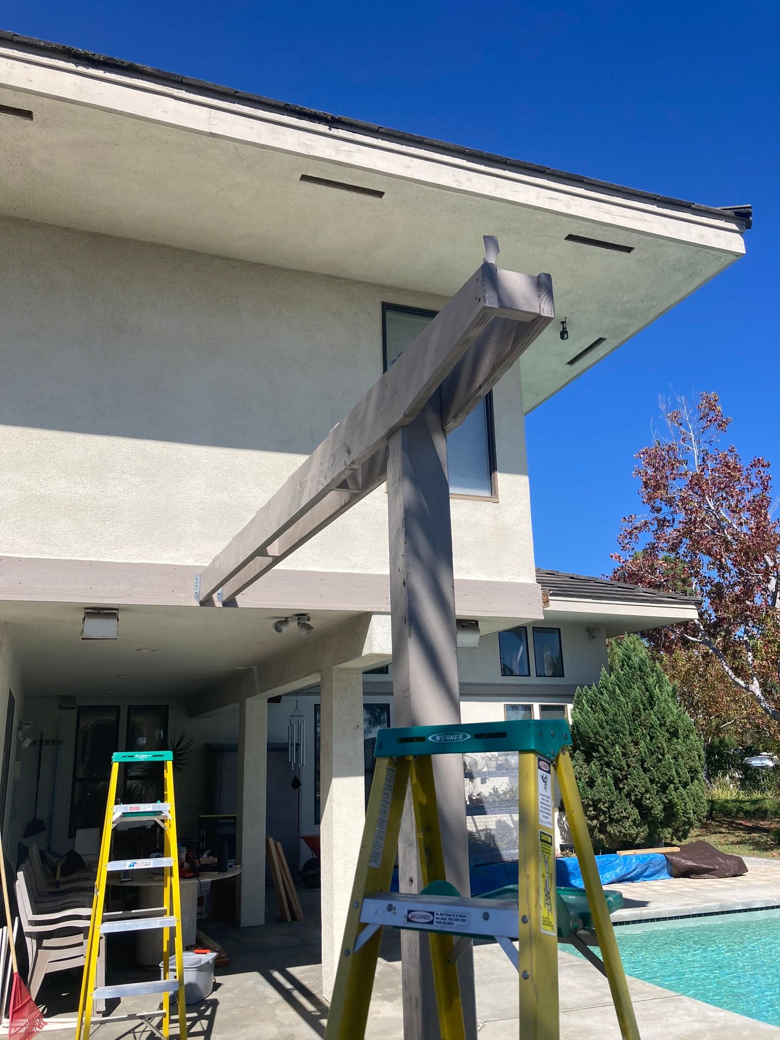 A ladder is sitting in front of a house next to a pool.