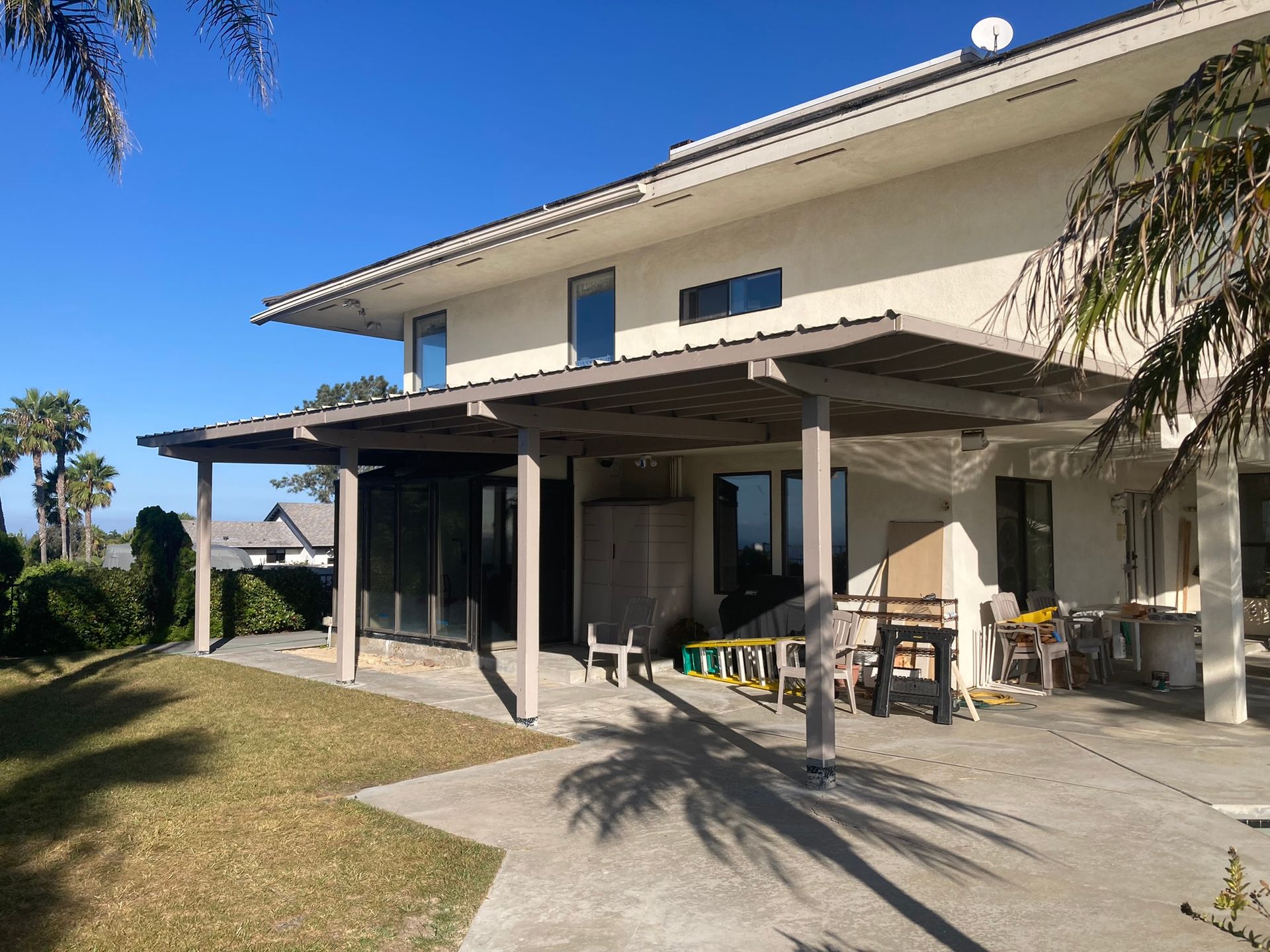 Back of a two-story beige house with a wooden pergola over a concrete patio on a sunny day.