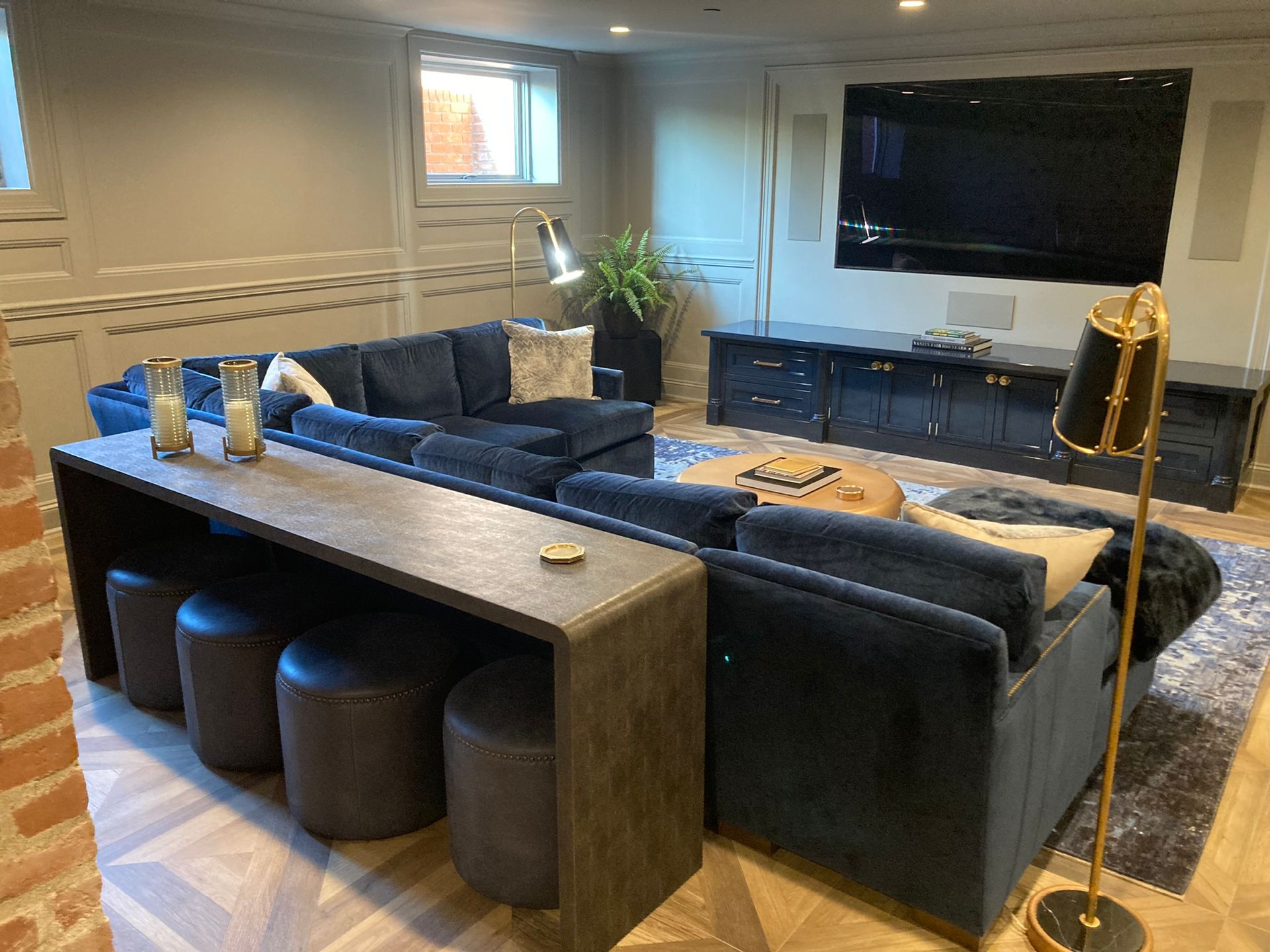 A modern basement living room with a large blue sectional, bar seating, and entertainment center.