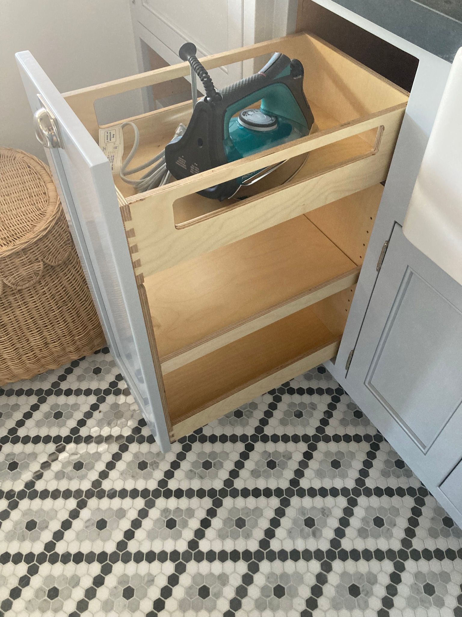 A pull-out cabinet with a teal iron inside, set on a patterned floor.