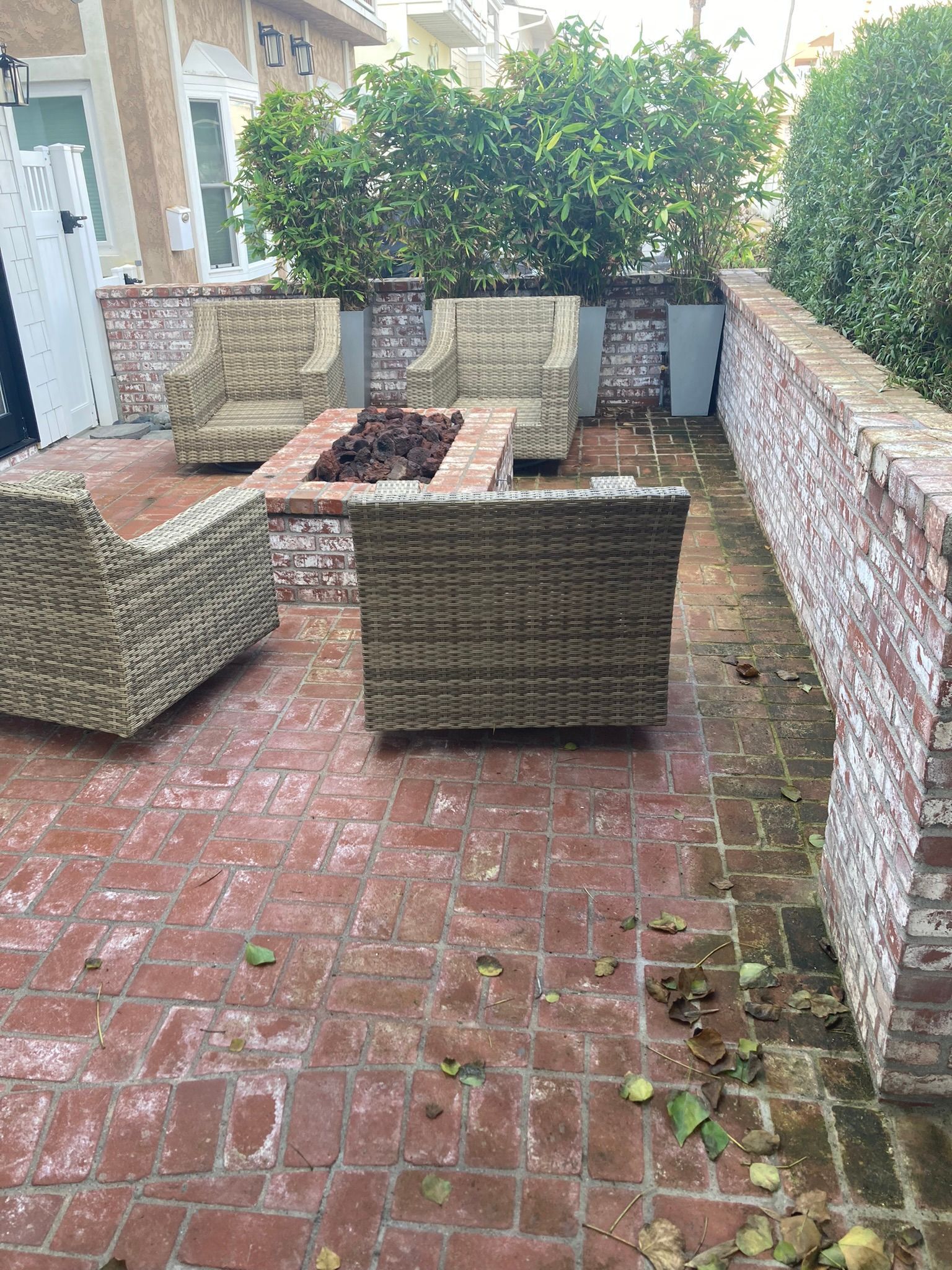 Brick patio with woven furniture around a fire pit, brick walls, and greenery.