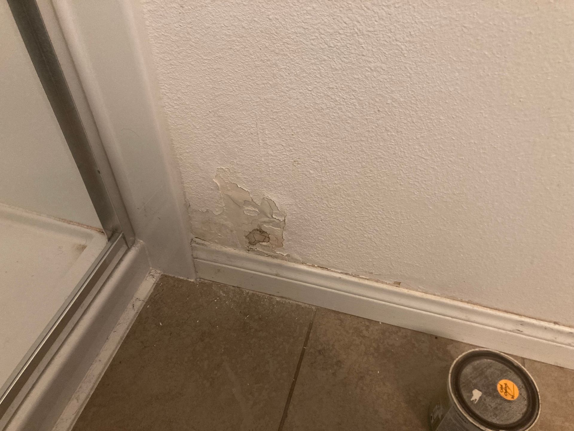 Water damage on a textured white wall near a shower door and floor.